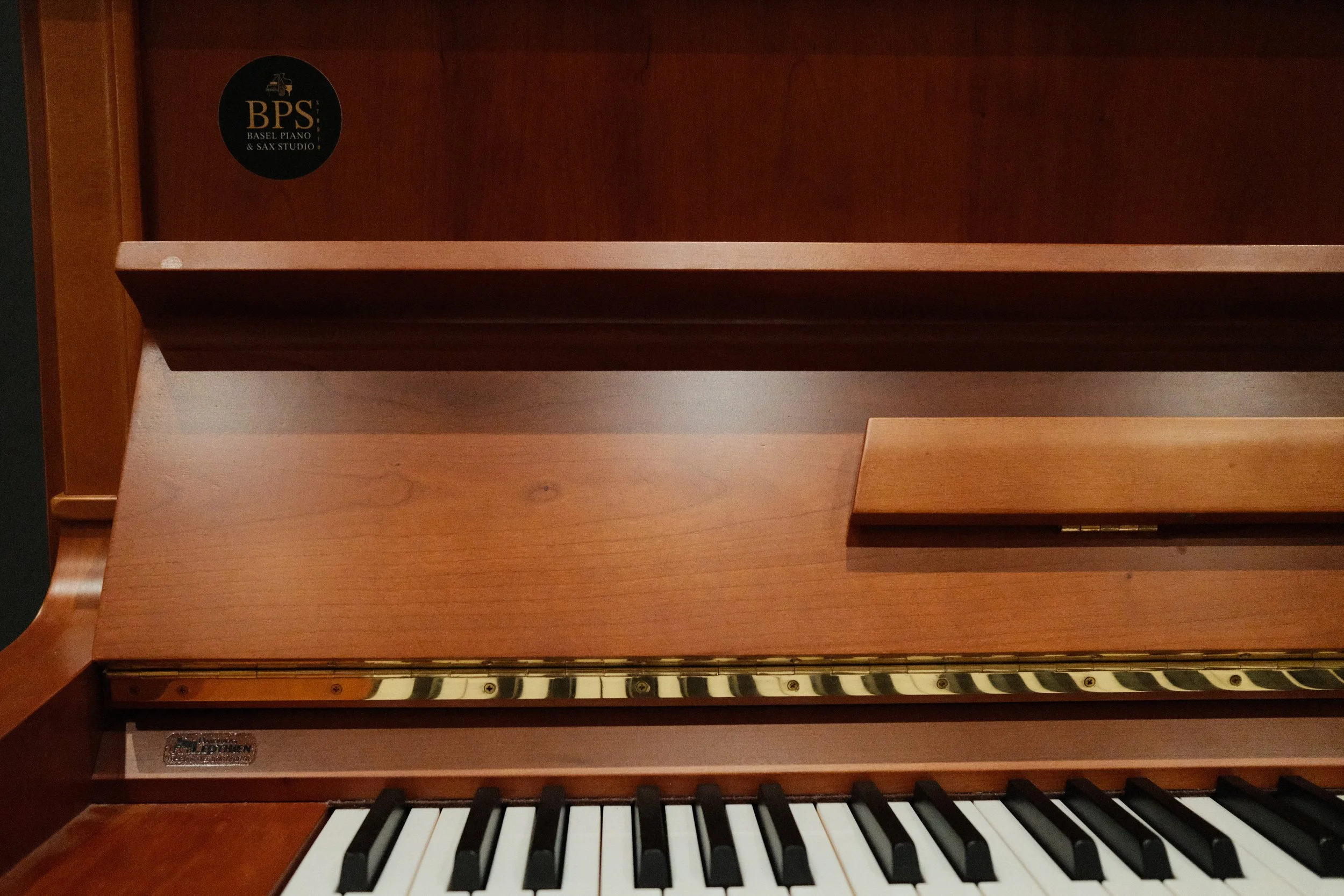 Close-up of an upright piano showing keyboard and wooden music stand.