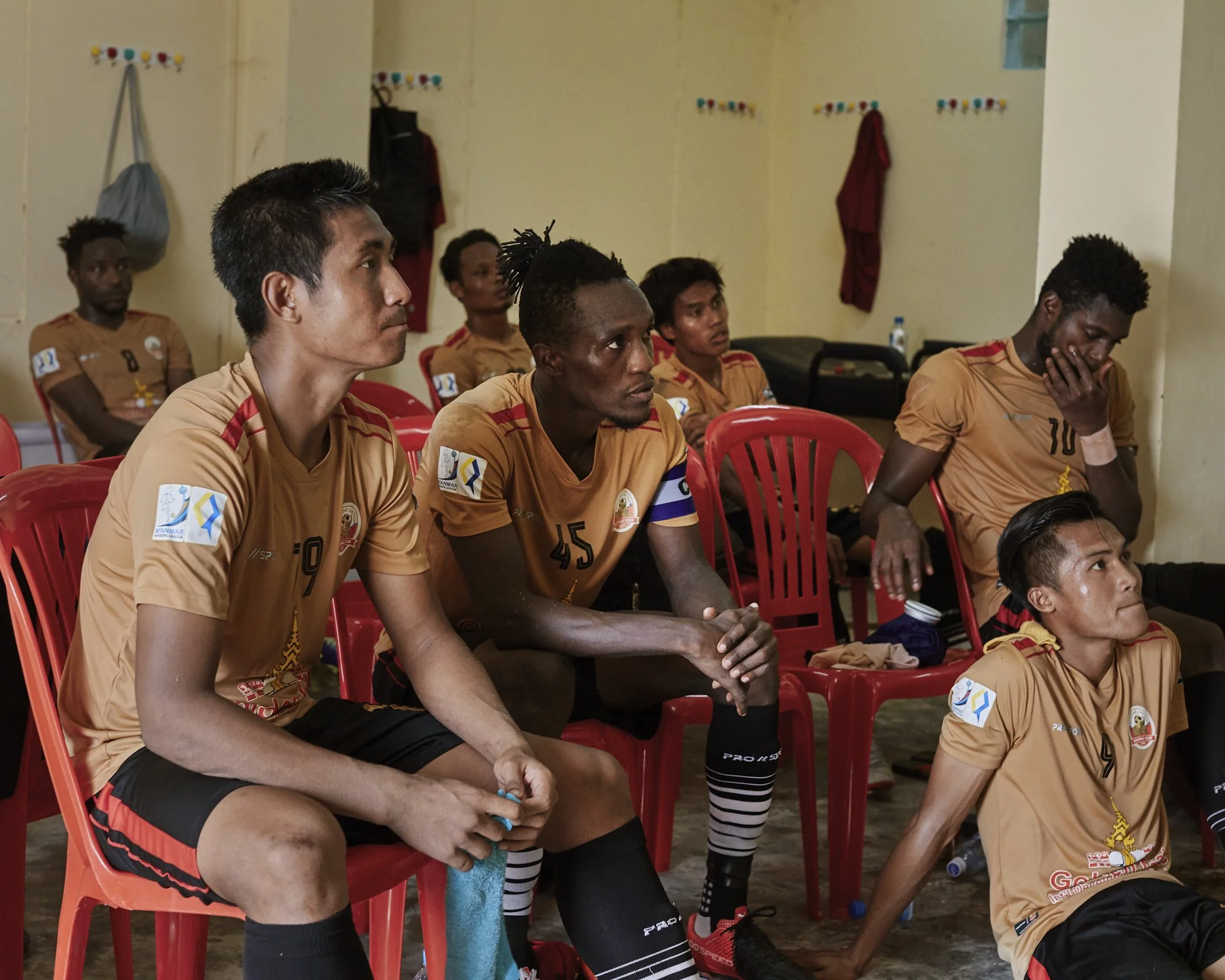 Les joueurs écoutent les consignes de l'entraineur lors de la mi-temps du match entre le Rakhine United et Hantharwady.  Dans un anglais chancelant, l'entraineur donne des consignes approximatives que les joueurs étrangers s'appliquent à déchiffrer.