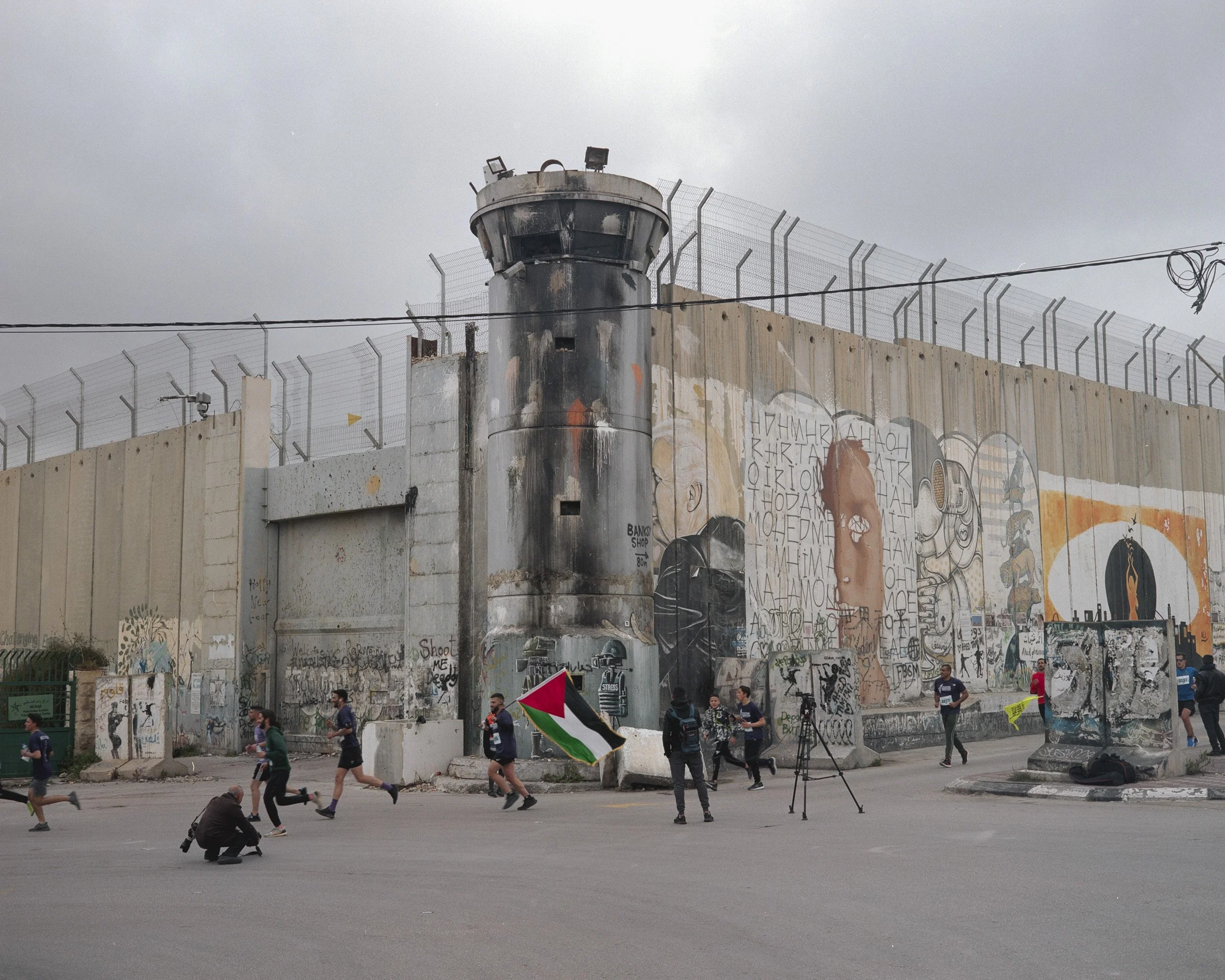 Runners of the Bethlehem Marathon pass in front of the separation wall, Bethlehem, March 18, 2022.