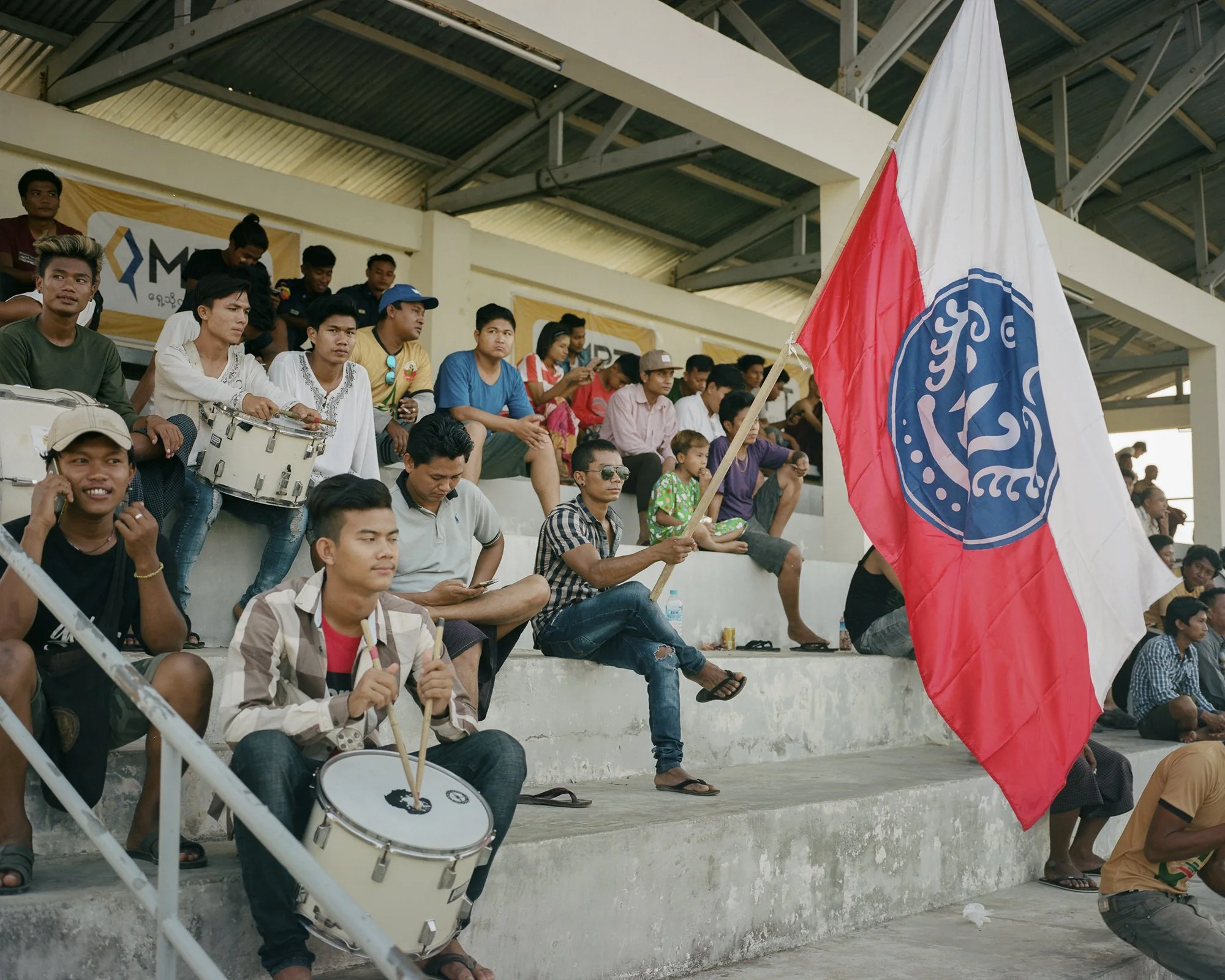 Supporters du Rakhine United FC dans les tribunes du stade Watharli.  Le drapeau est celui de le la région de l'Arakanoù la guerre civile entre autonomistes arakanais et l'armée régulière a repris depuis le début de l'année. 31 mars 2019