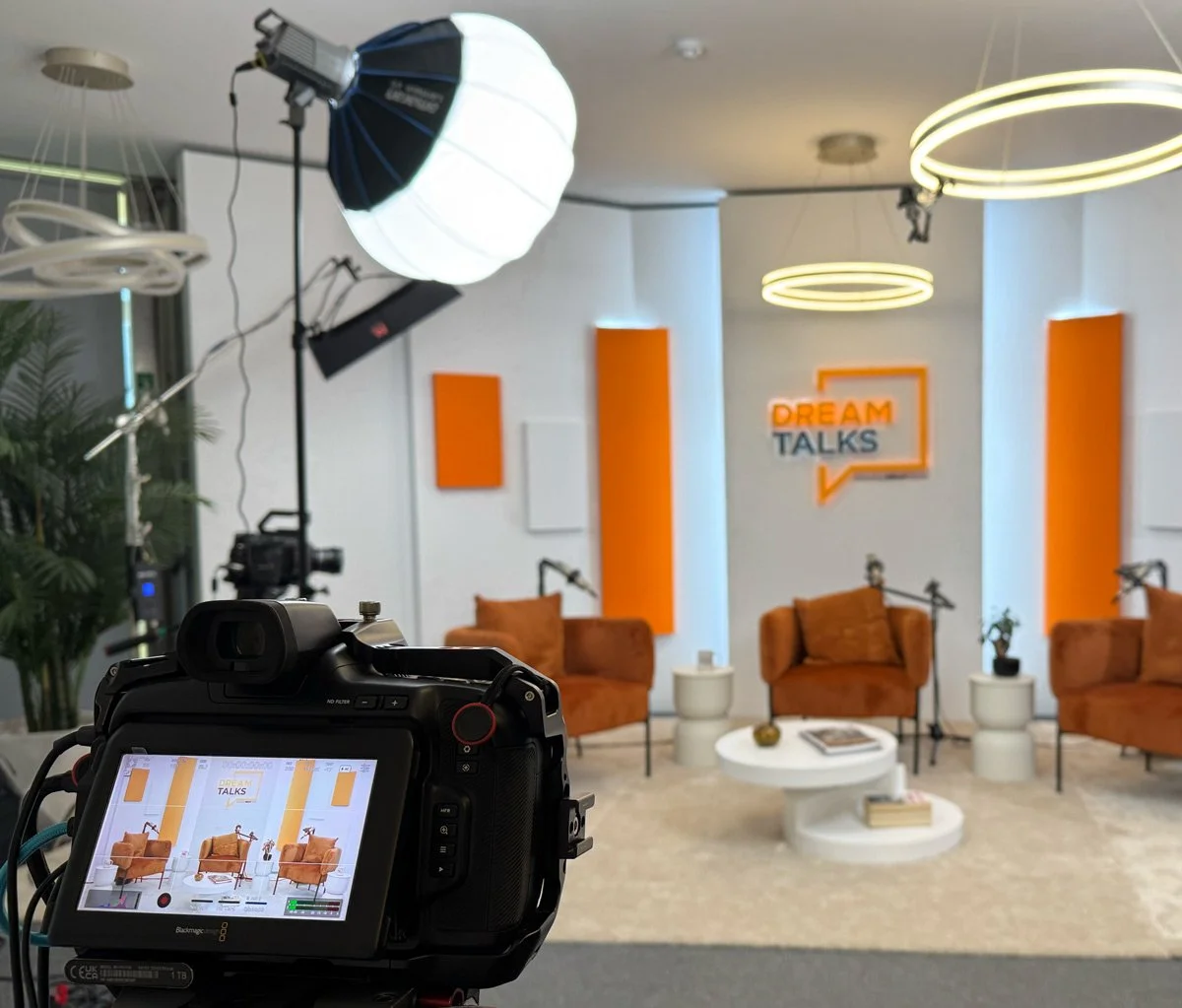 Estúdio de gravação com iluminação, câmeras, e móveis de sofá e mesa, decorado para um programa chamado 'Dream Talks'.