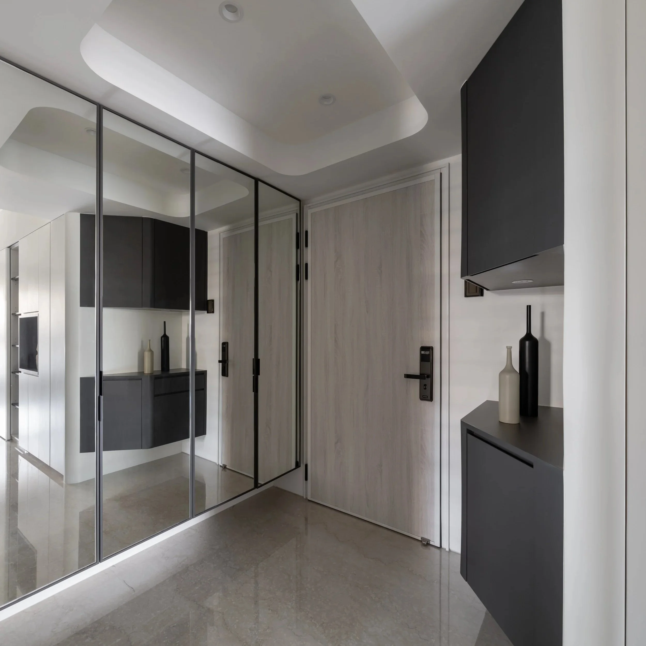 Modern interior space with a large mirrored sliding door, black and white cabinets, decorative vases, and a sleek black range hood on the wall.