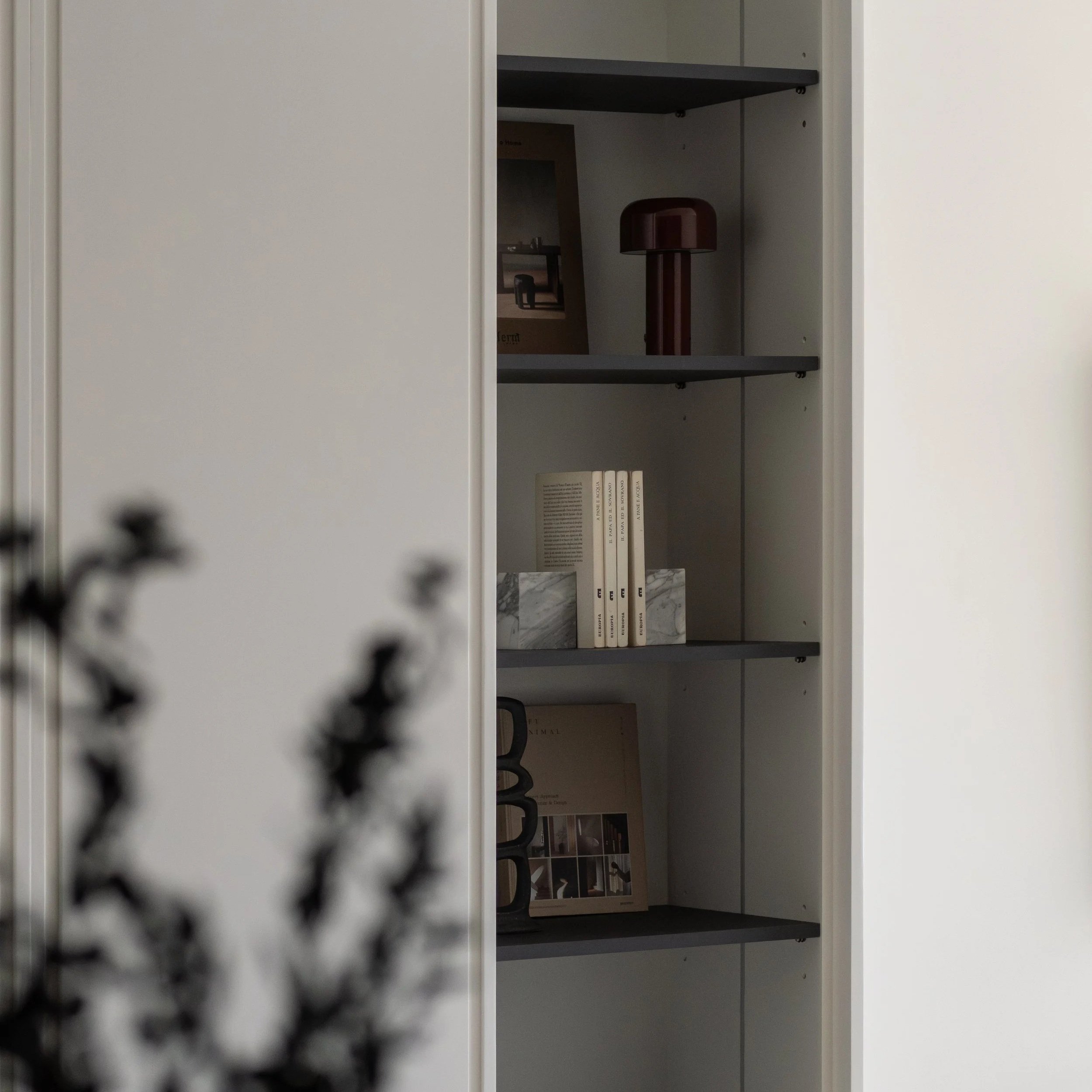 Open grey bookshelf with books and magazines inside, seen through a perforated metal panel.