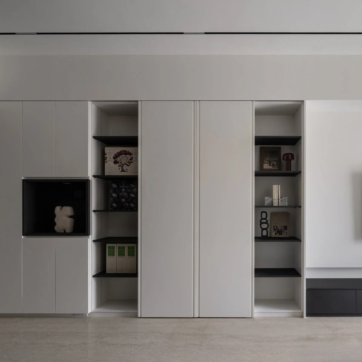 Modern white built-in wall unit with open black shelves displaying decorative items and books.