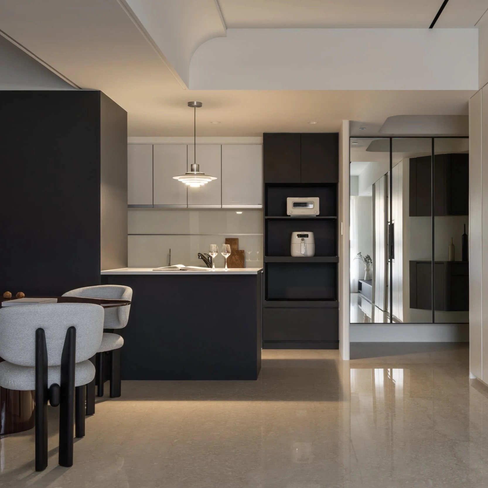 Modern kitchen and dining area with black and white cabinetry, a hanging pendant light, and a glass partition.
