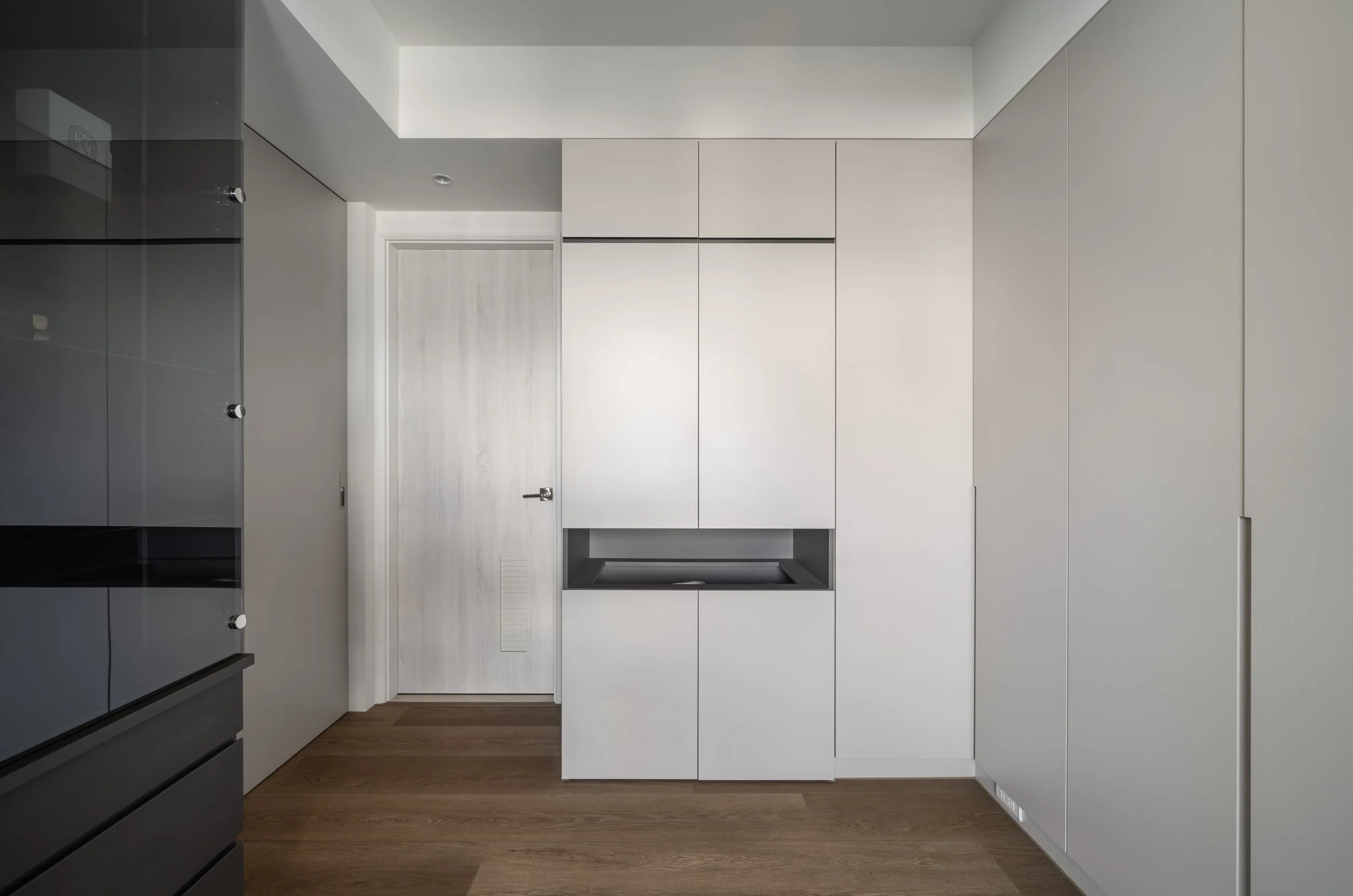Modern kitchen interior with white cabinetry, wooden floor, a door, and a skylight ceiling.