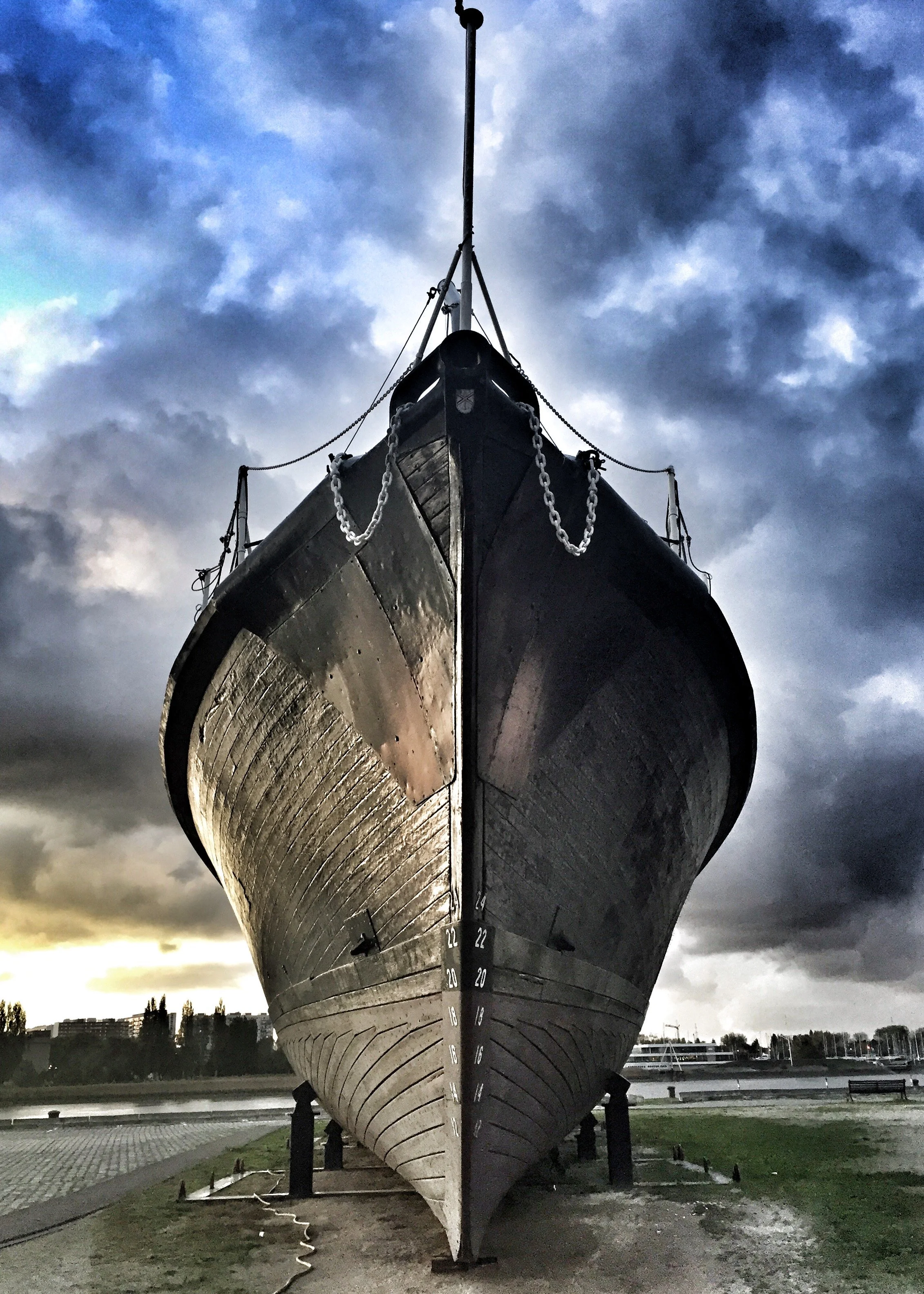 Front view of a large black ship in a dry dock with a cloudy sky in the background.