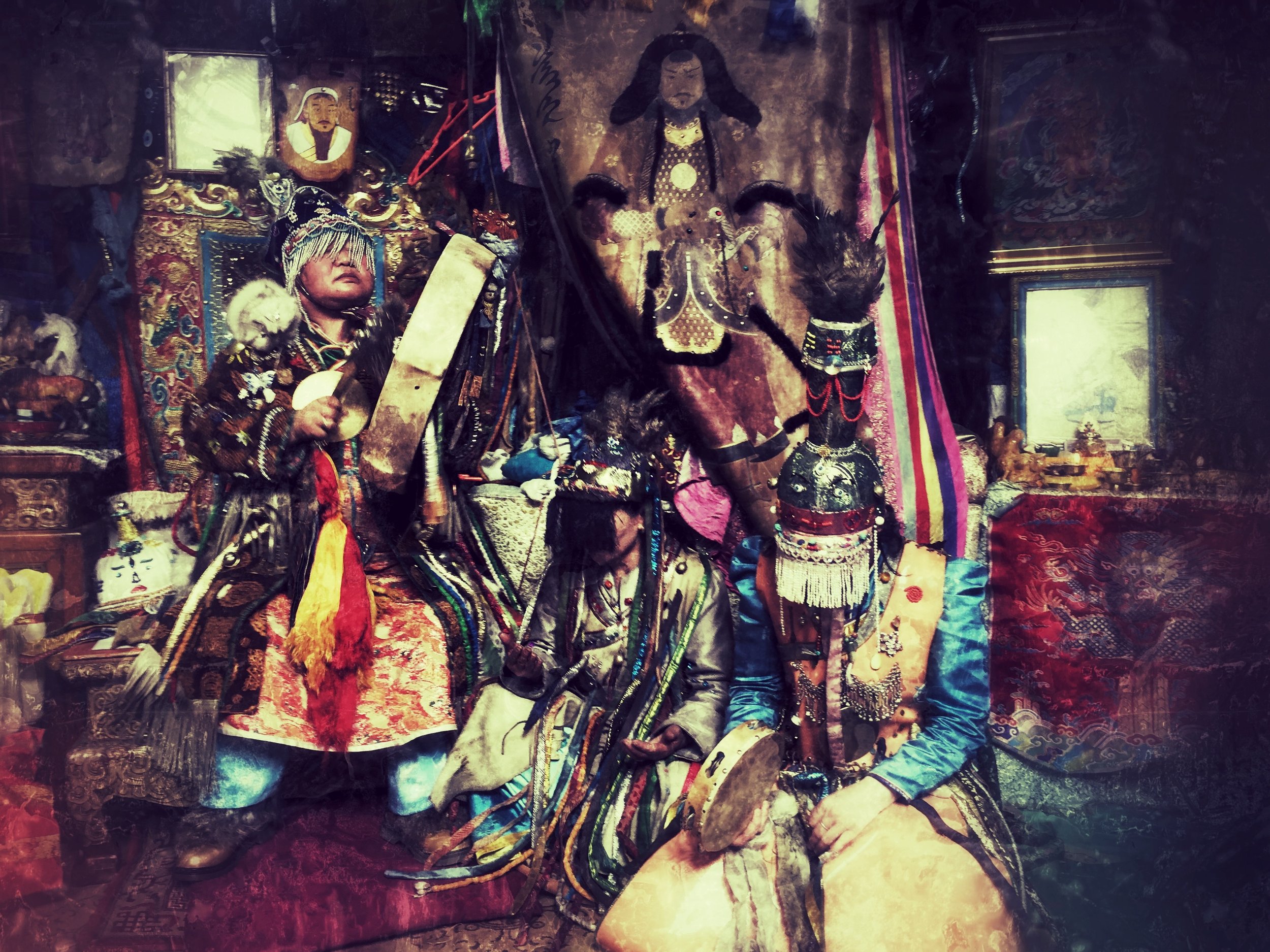 A collection of traditional and religious artifacts, including a portrait, masks, and decorated objects, displayed in a shrine or altar setting with embroidered textiles.