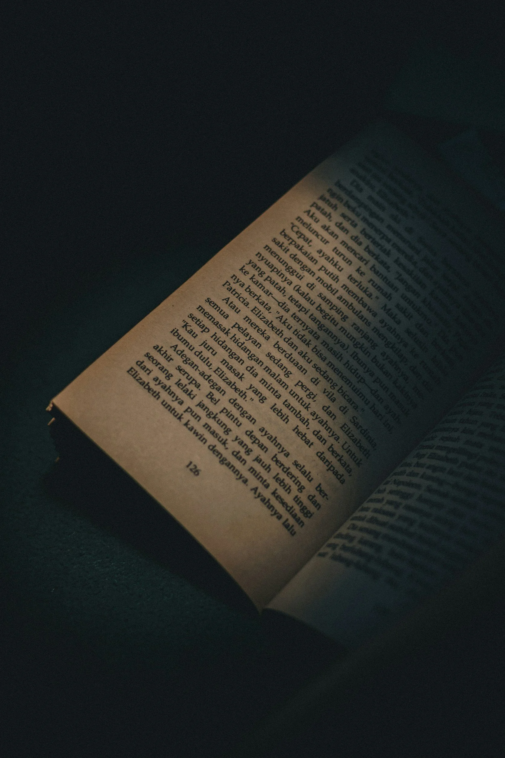 Close-up of an open book with text written in Indonesian on a dark background.