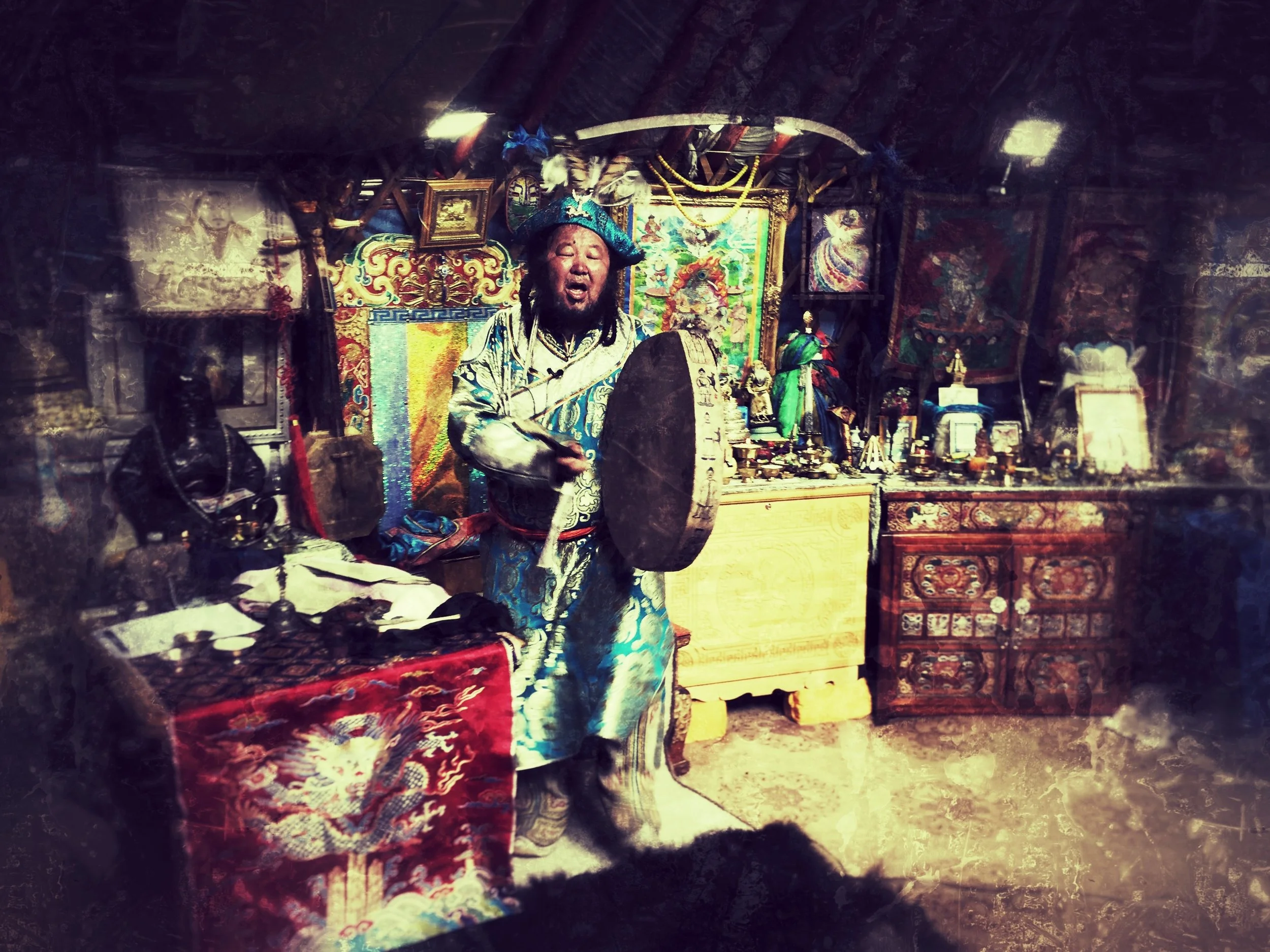 A person dressed in traditional, colorful, and intricate clothing, standing amidst various religious and cultural artifacts in a dimly lit room filled with paintings, statues, and textiles.
