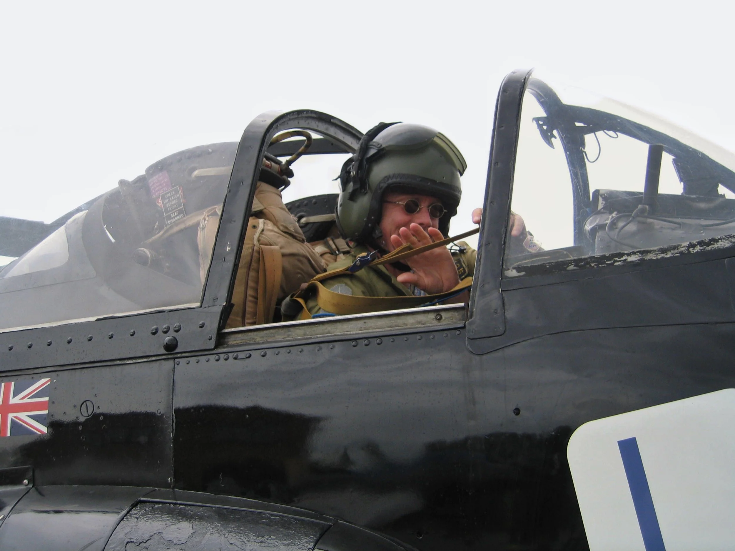 Military pilot wearing helmet and sunglasses sitting inside fighter jet cockpit, preparing for flight.