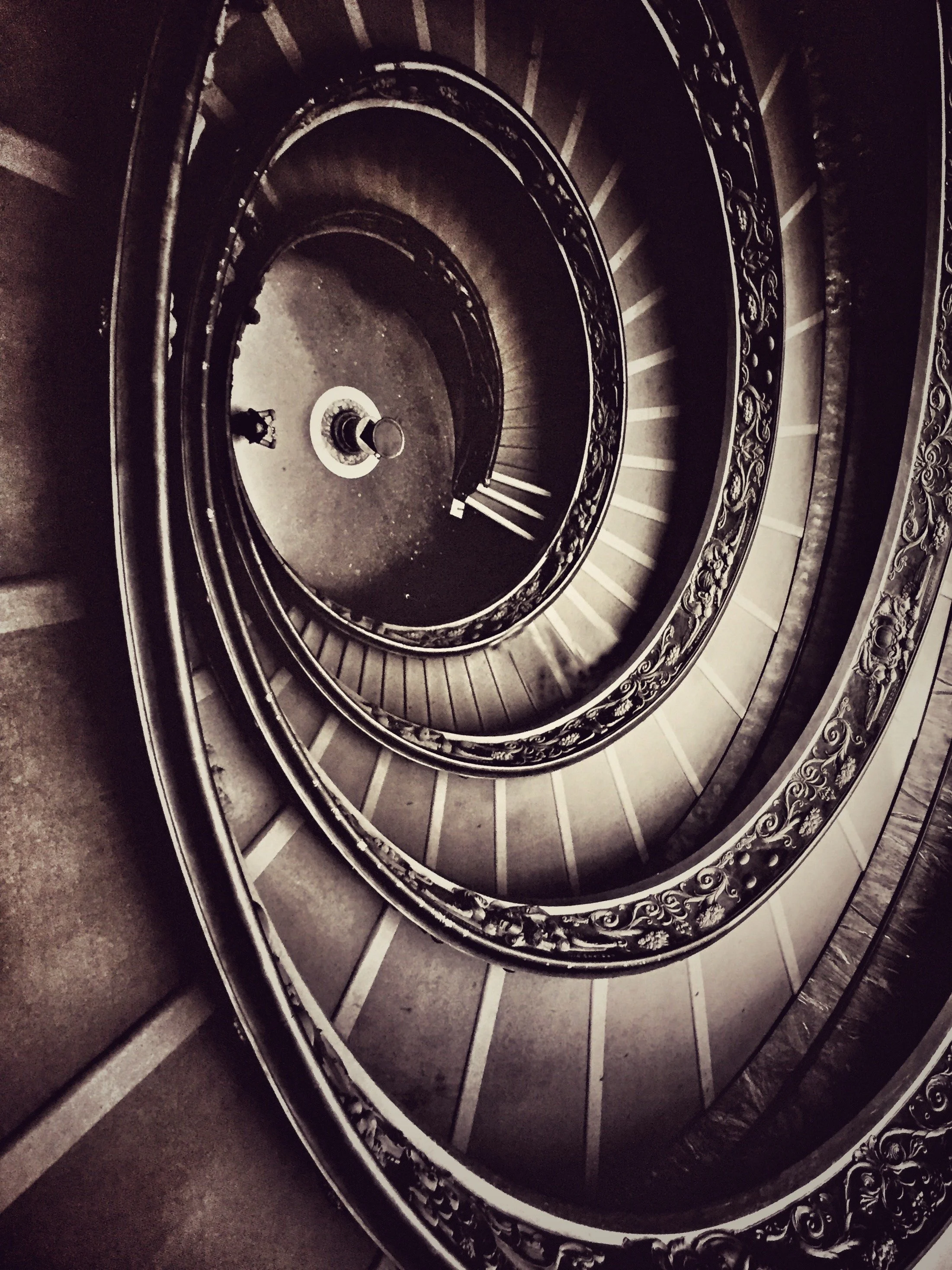 A spiral staircase with ornate black metal railing and dark steps, viewed from above.