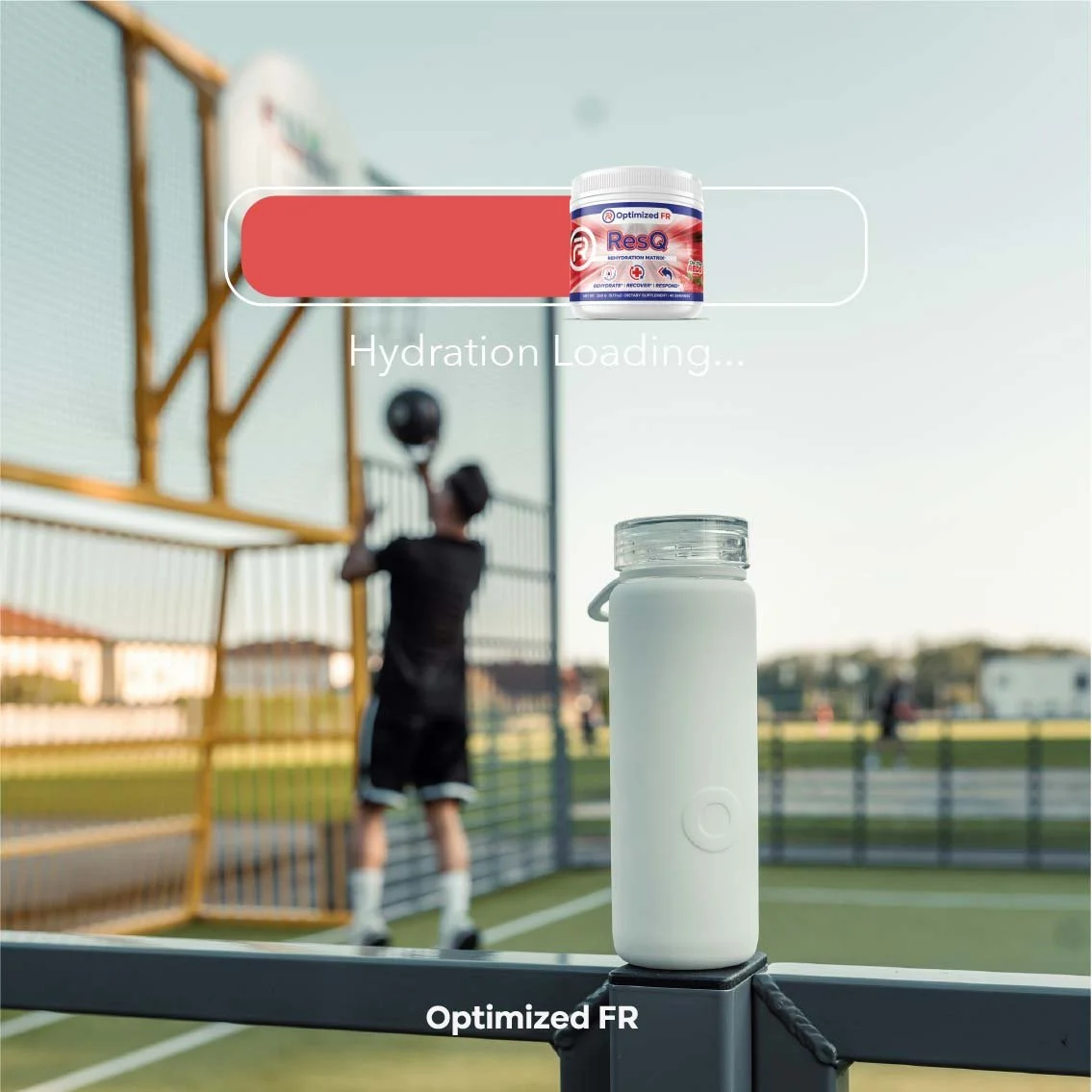 Water bottle placed on a railing at a sports field, with a blurred person during a basketball game in the background.