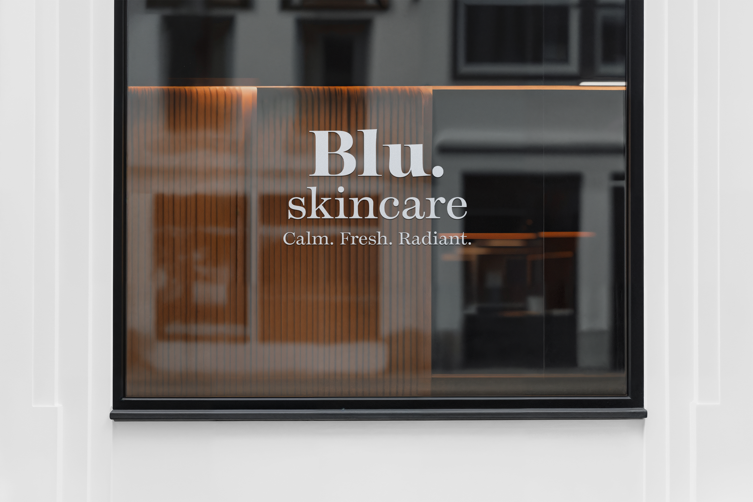 Close-up of a glass door with the words 'Blu. Skincare' and the slogan 'Calm. Fresh. Radiant.' printed on it, with a warm wood interior visible through the glass.