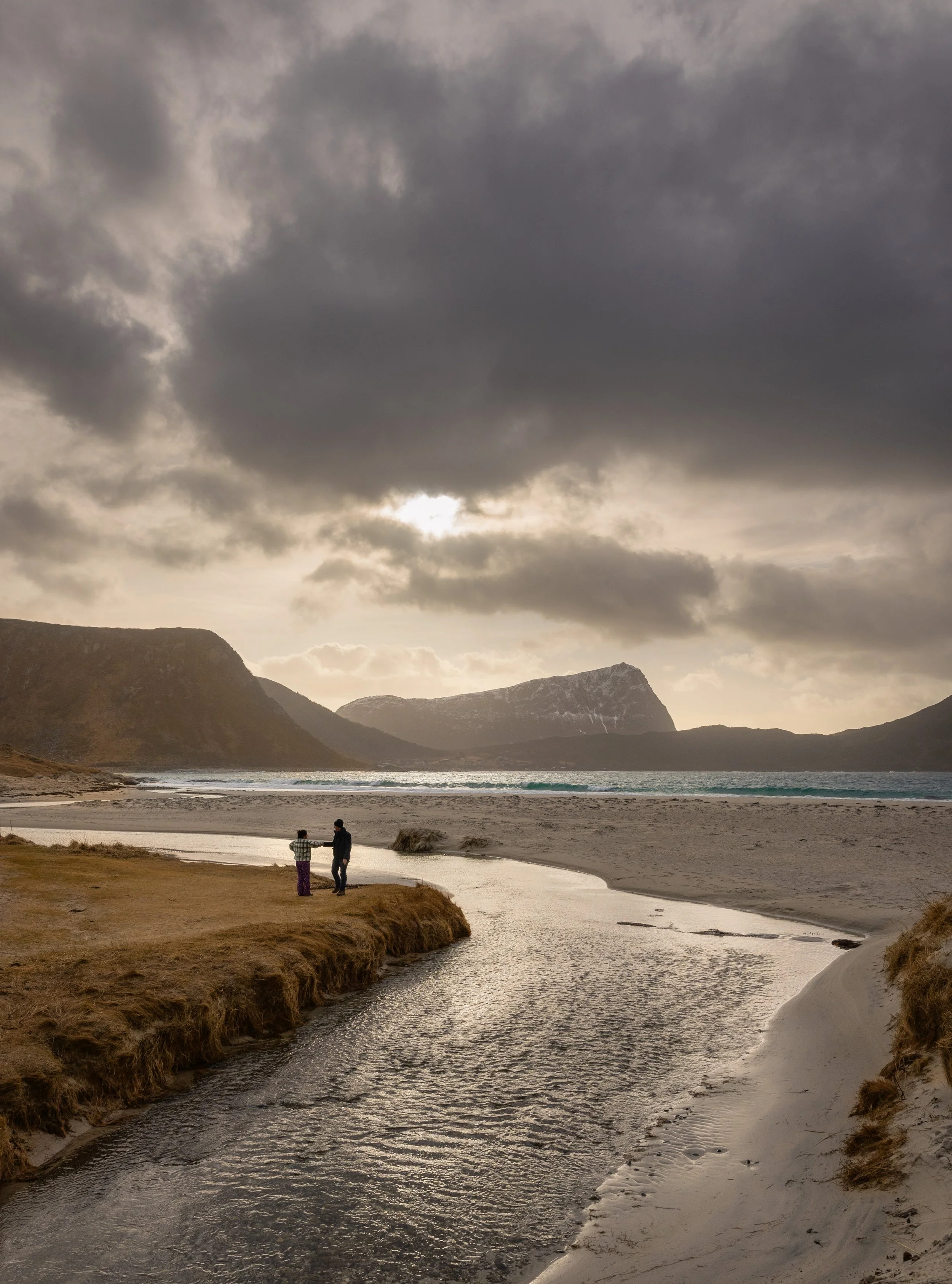 Two small figures beside a stream crossing a beach under broken cloud, Lofoten, Norway