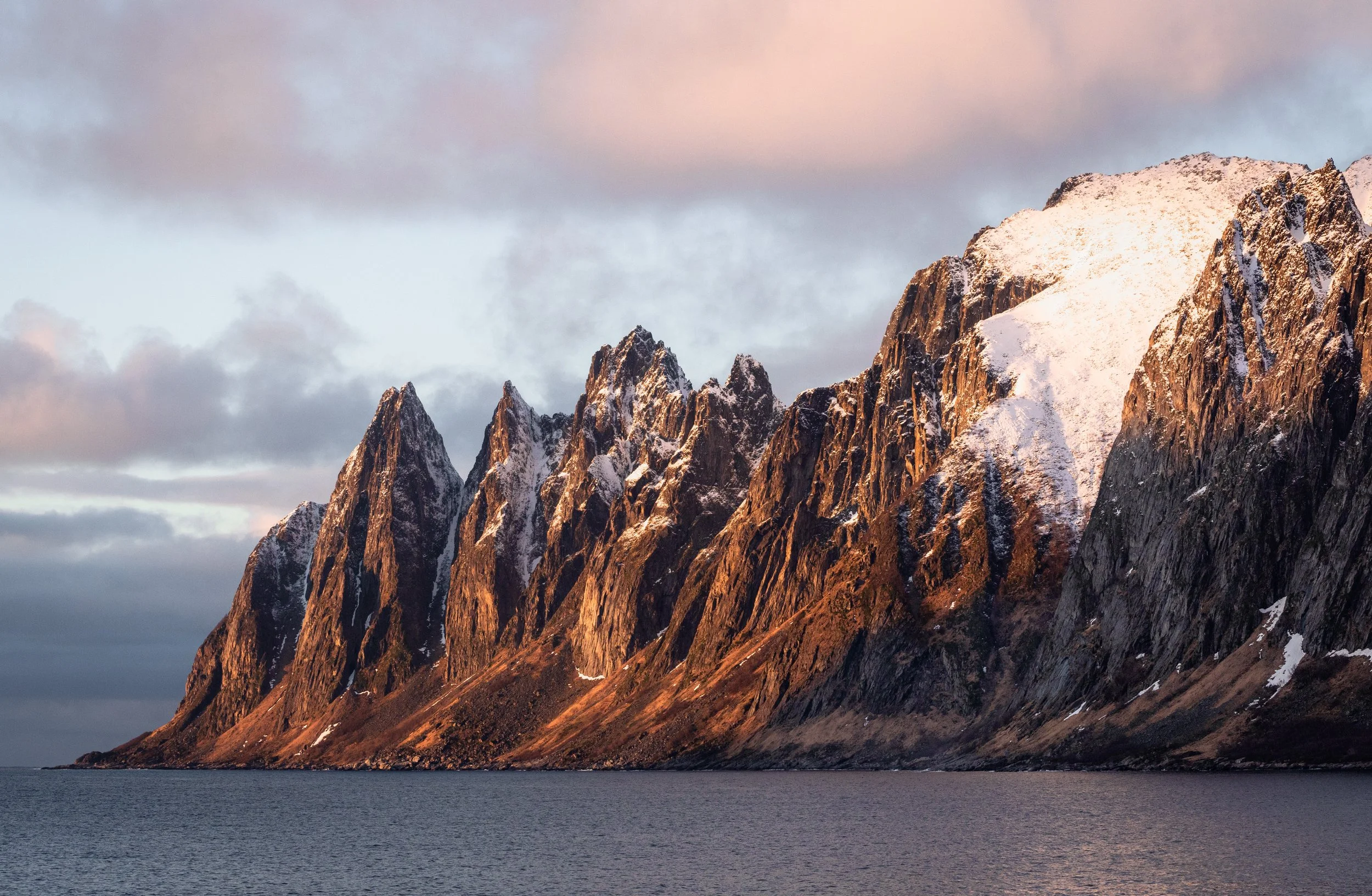 The serrated ridge of the Okshornan peaks catching first light above the fjord, Senja, Norway — the Devil's Teeth, a wall of gabbro rising straight from the water.