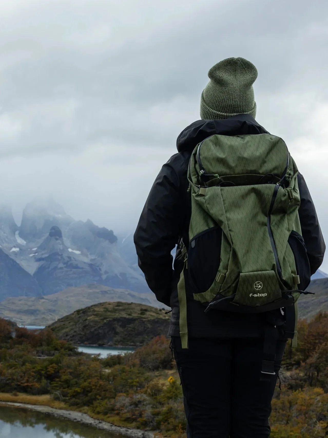 Vasiliki Kelaidi with an f-stop camera pack above a lagoon in Torres del Paine, Chilean Patagonia — the Cuernos under cloud, as they are most days here.
