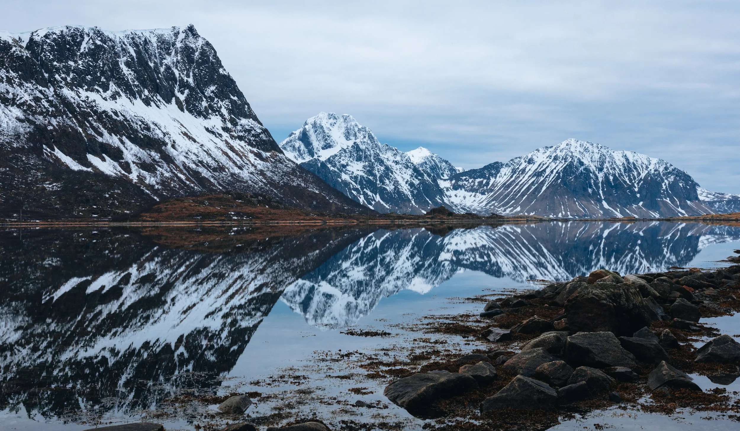 Snow-covered peaks mirrored in still water at low tide, Lofoten, Norway