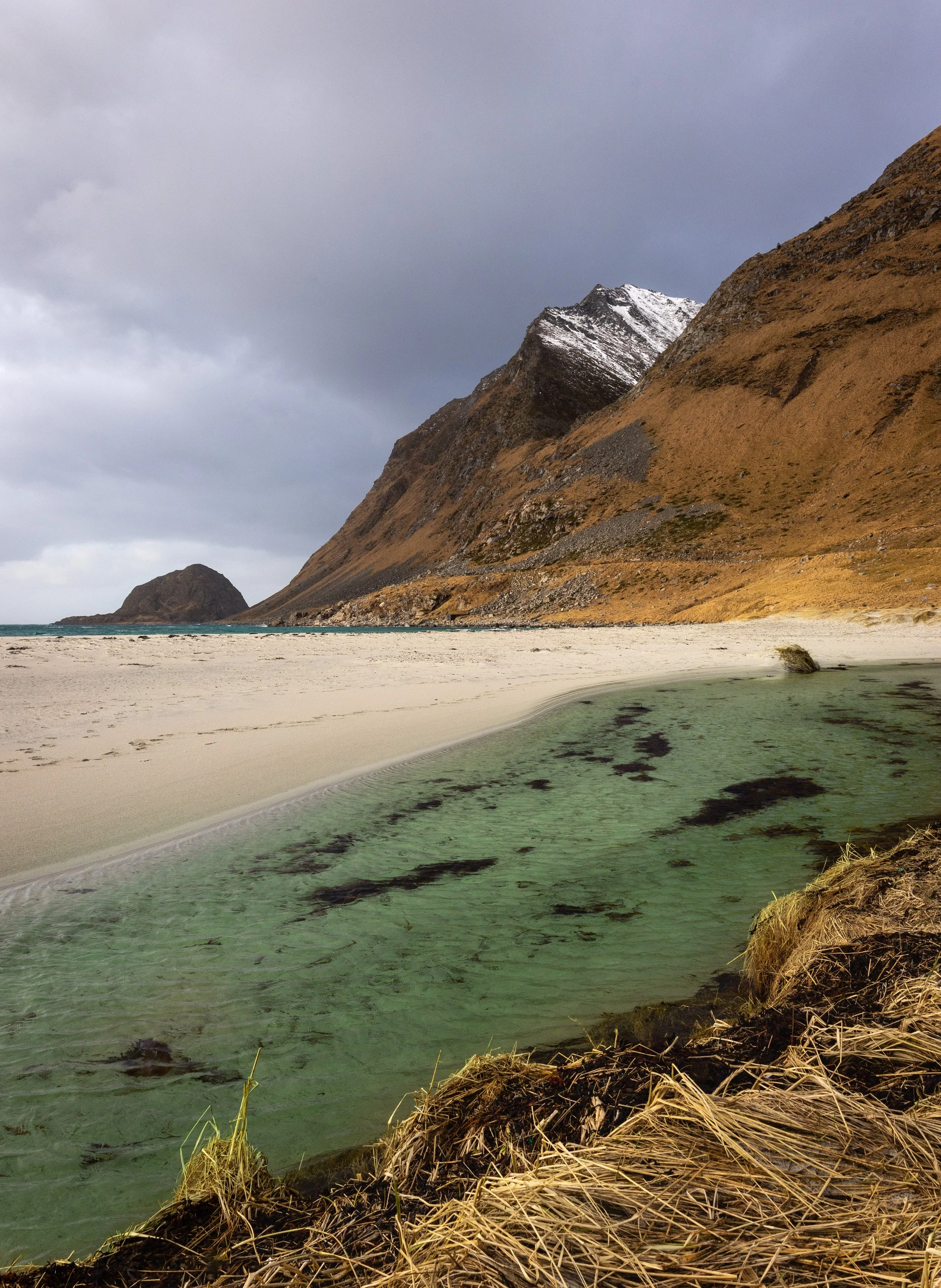 White sand beach with turquoise shallows below a snow-dusted peak, Lofoten, Norway