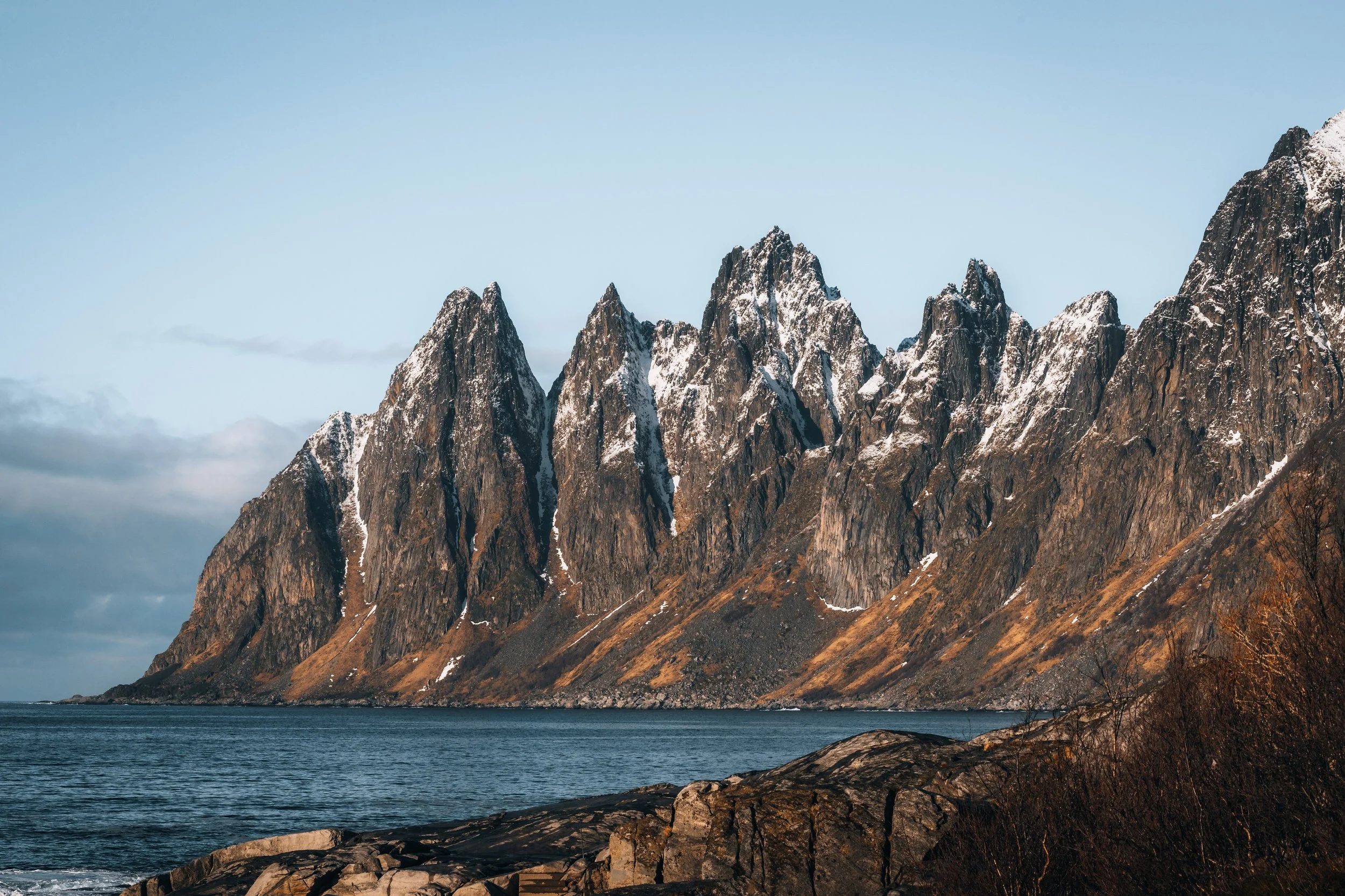 The Okshornan ridge across the fjord from a rocky foreshore, Senja, Norway — a line of separate peaks rather than one summit, which is how the range got its name.