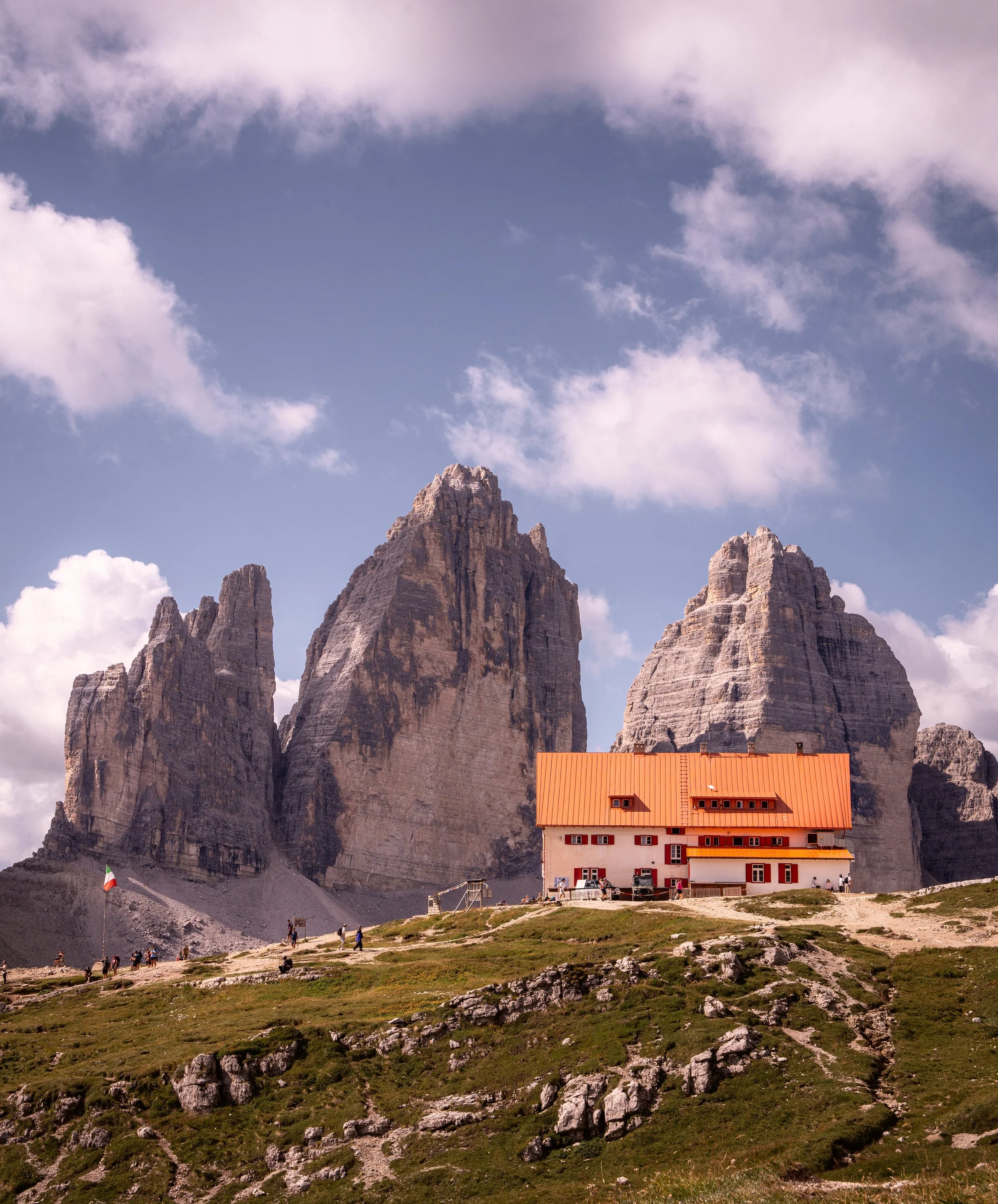 The orange roof of a mountain hut (rifugio Locatelli) below the three towers of Tre Cime di Lavaredo, Dolomites, Italy — the saddle here is the meeting point of the circular route around the massif, walked by thousands each summer and empty within an