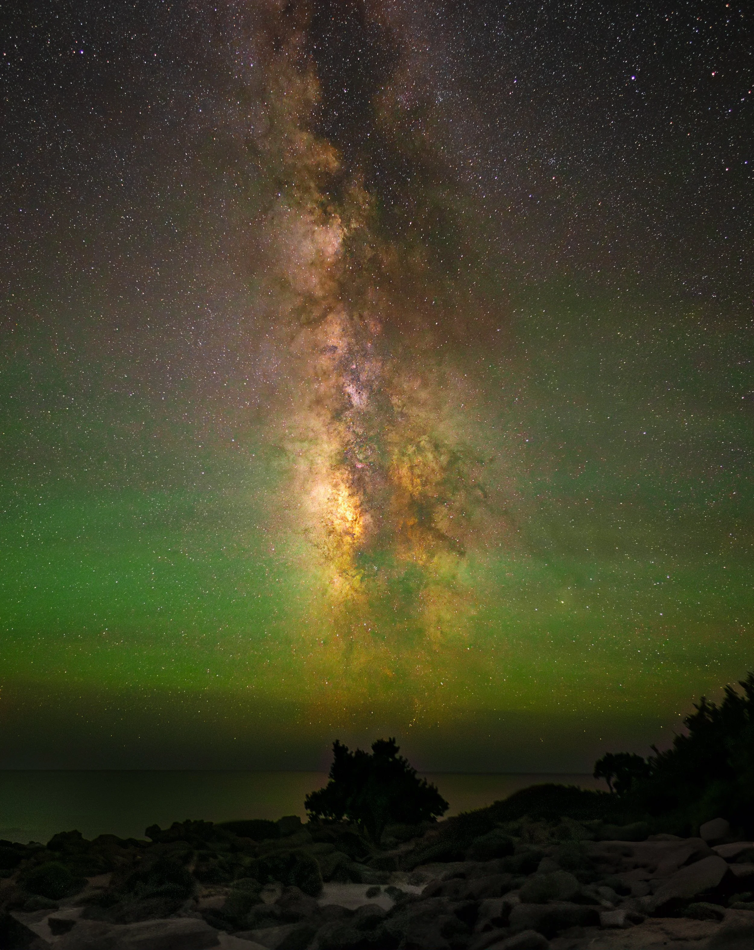 Milky Way core rising above a rocky Cretan shoreline with green airglow along the horizon, Crete, Greece