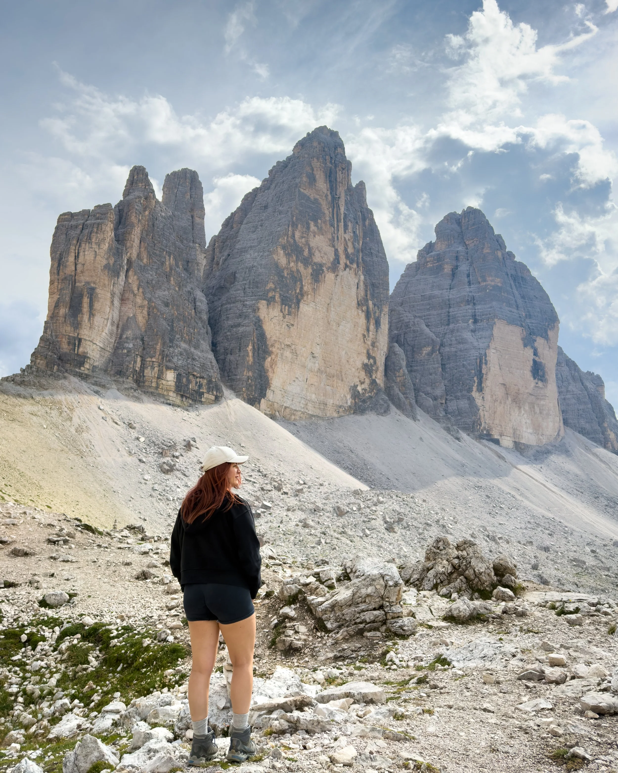 Vasiliki Kelaidi below Tre Cime di Lavaredo, Dolomites, Italy — the scree at the base is shed limestone, the towers losing themselves a fragment at a time to the freeze-thaw cycle that shapes the whole range.