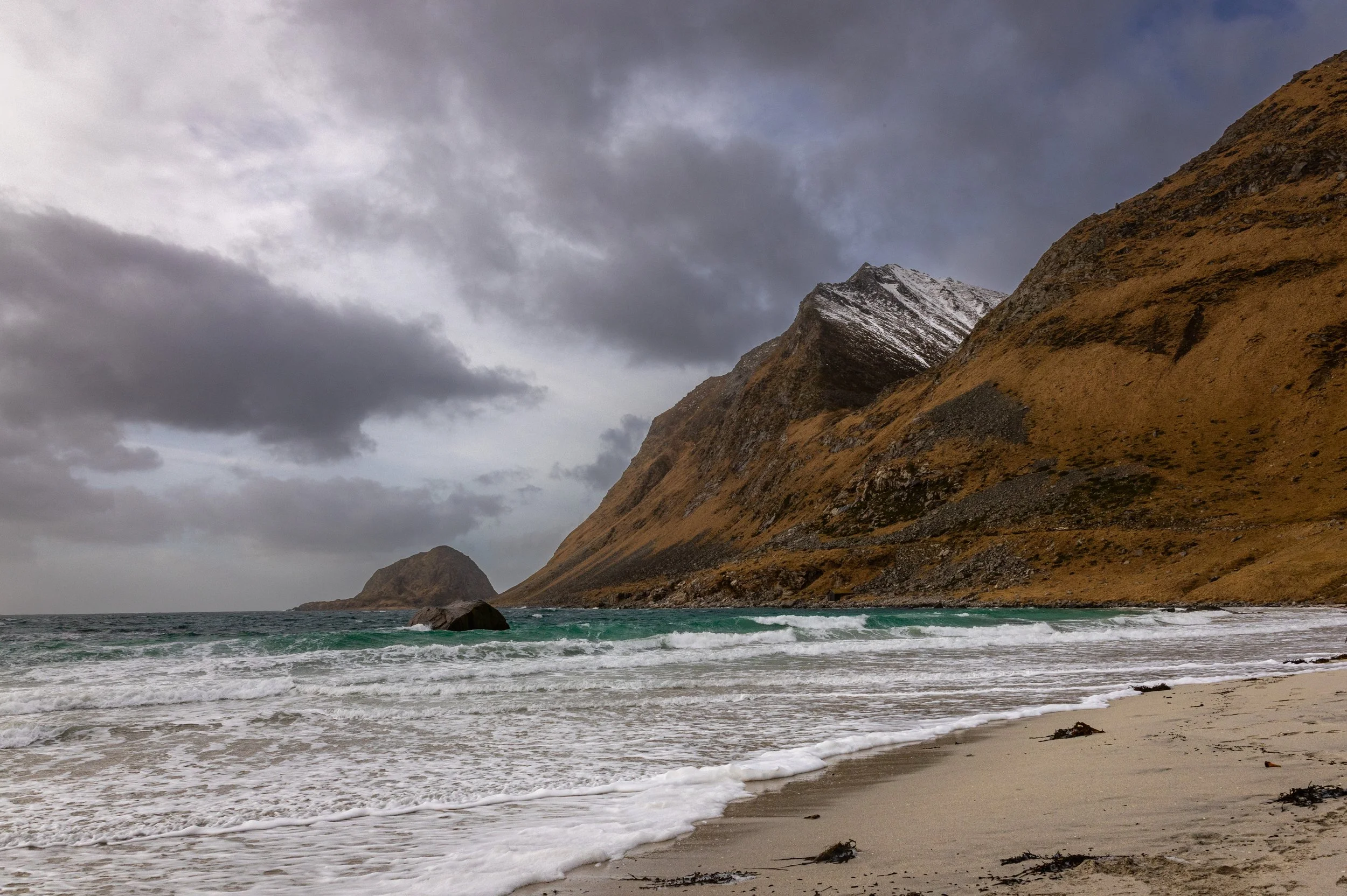 Waves breaking on a sand beach below a steep ridge under dark cloud, Lofoten, Norway