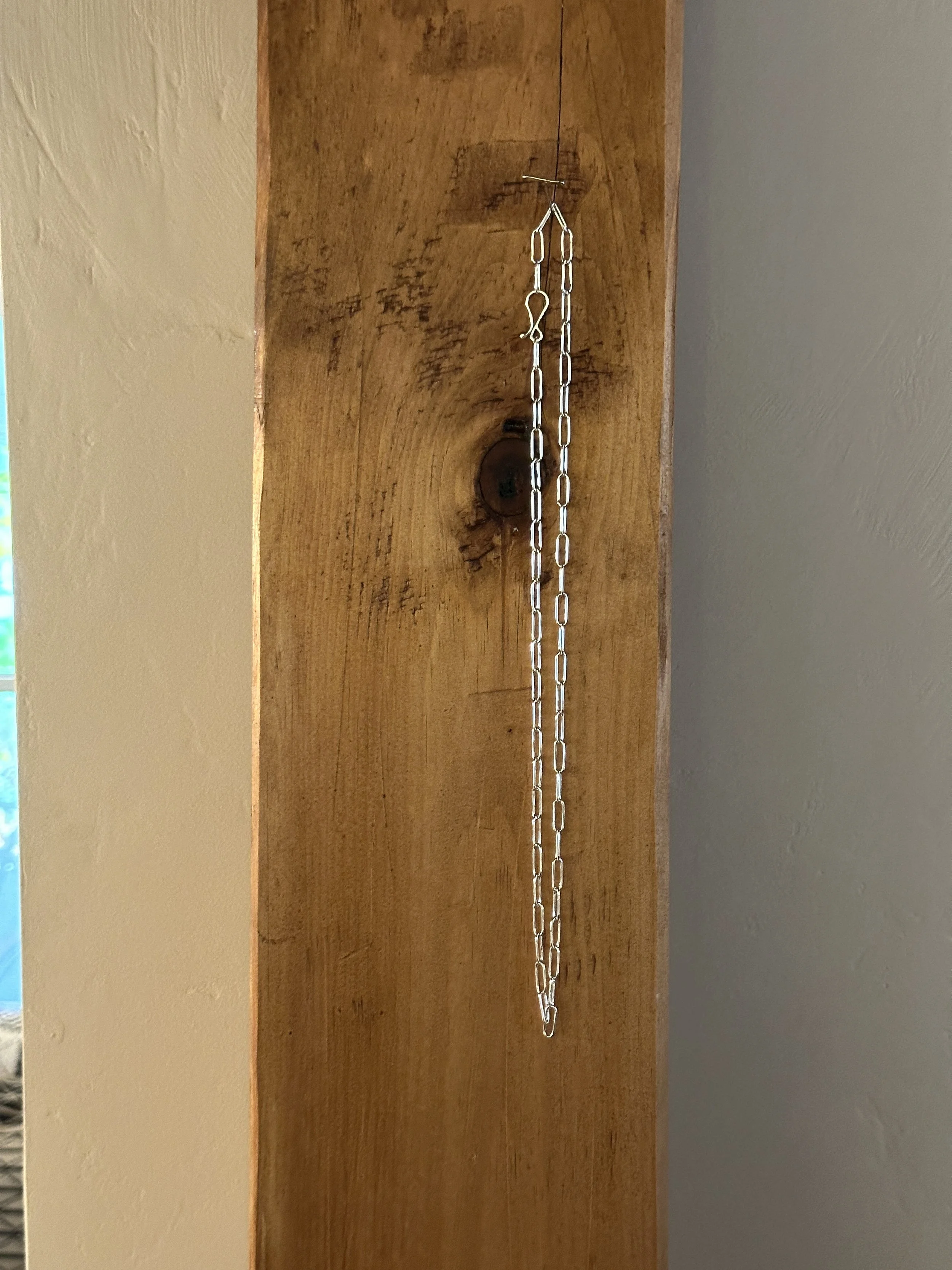 Full length of a handmade sterling silver chain necklace hanging on a timber post.