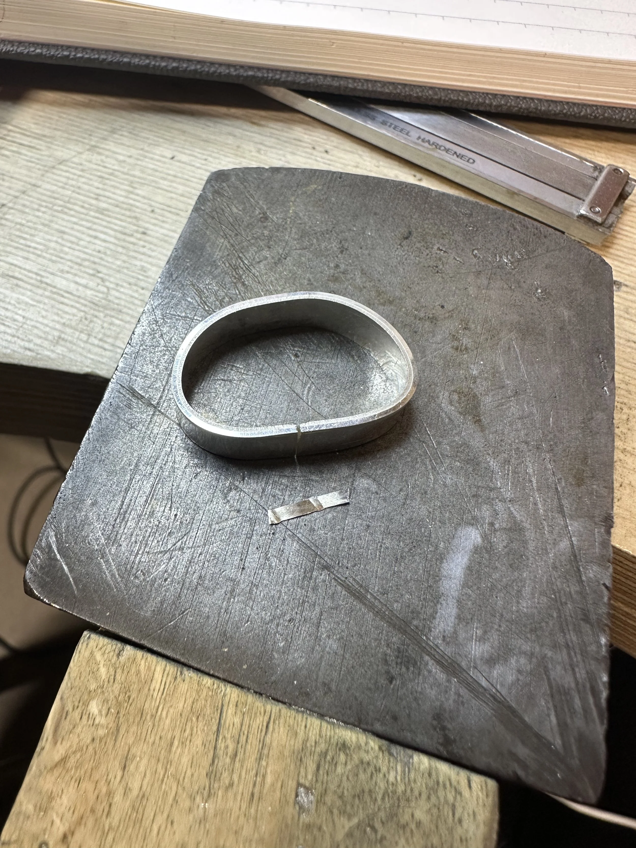 A silver ring on a jeweler's anvil with a strip of hard solder laying next to it.