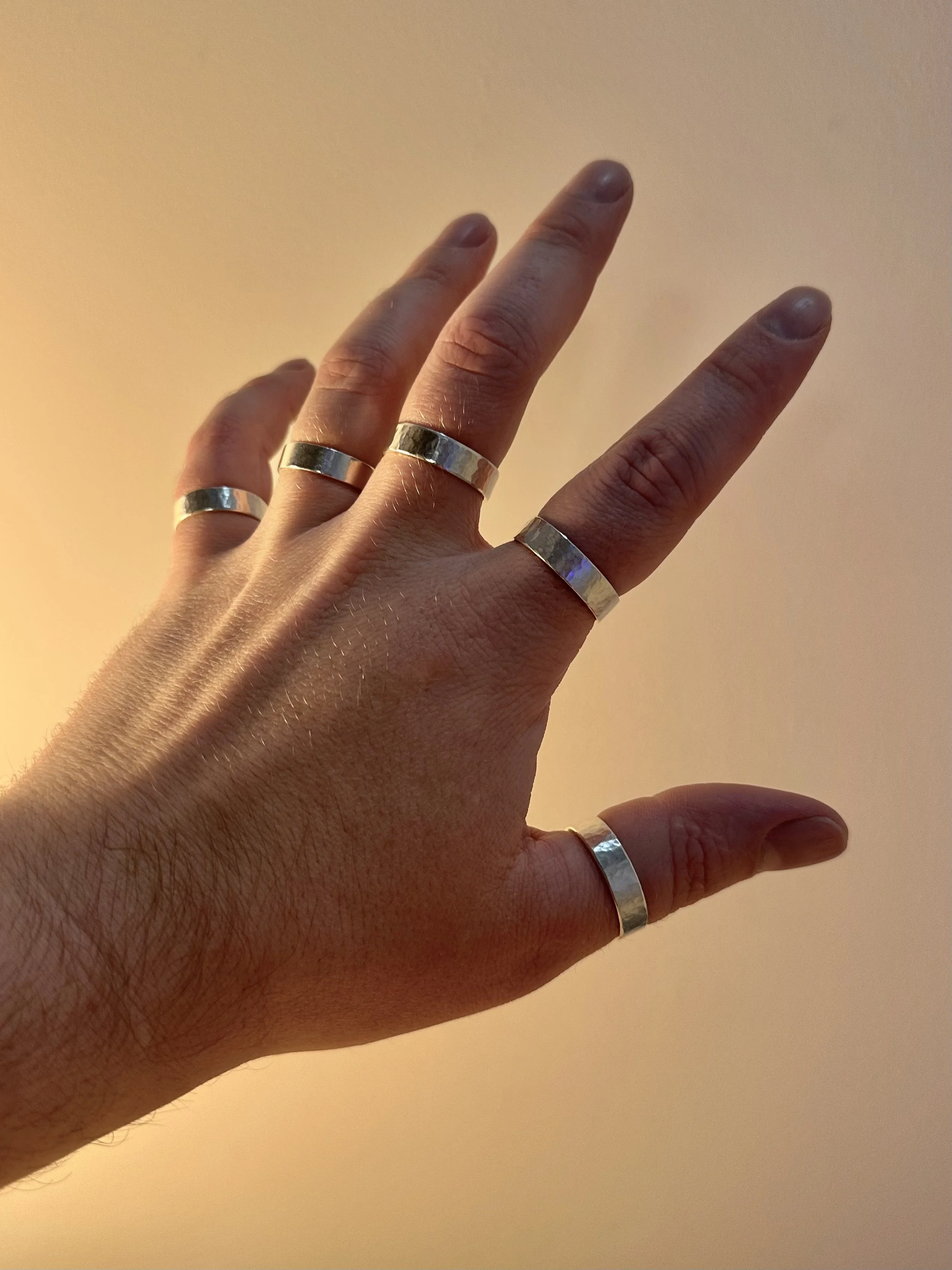 A hand on a plain background with one silver ring per finger.