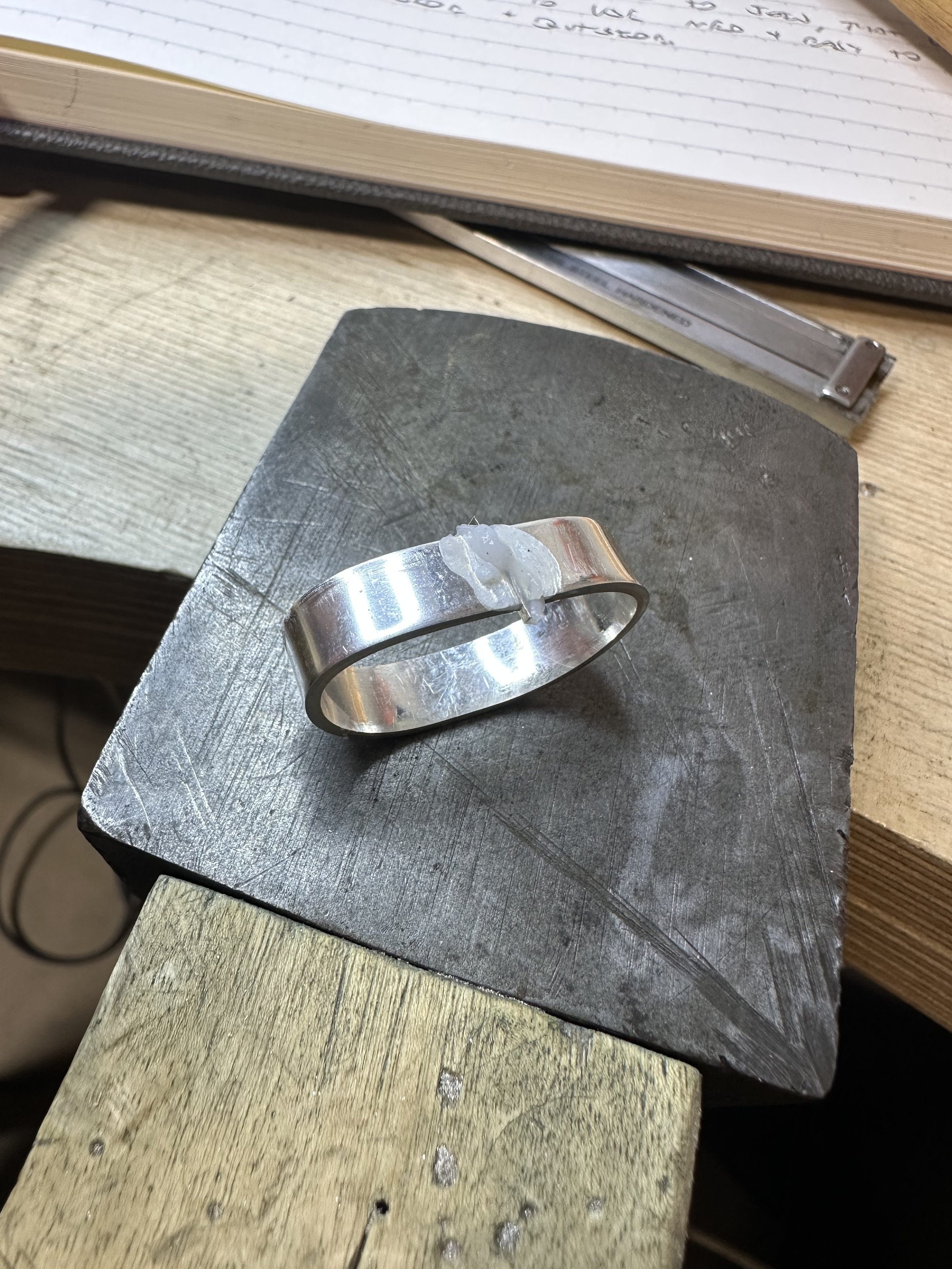 A silver ring on a jeweler's anvil with flux applied to the joint and the solder placed between the two ends.