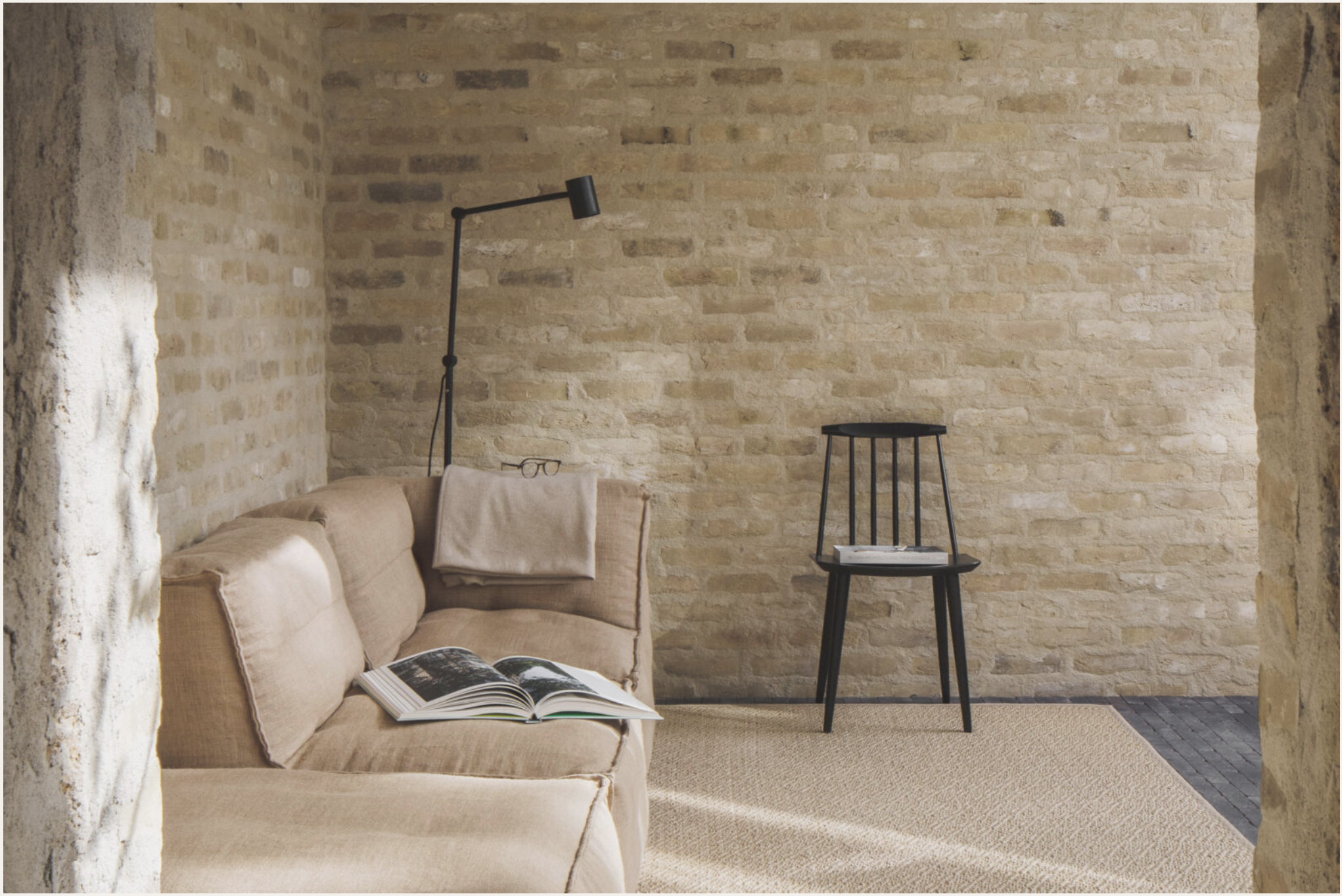 Living room with beige sofa, open book, stone walls, black floor lamp, small black side table with magazines, and beige carpet.