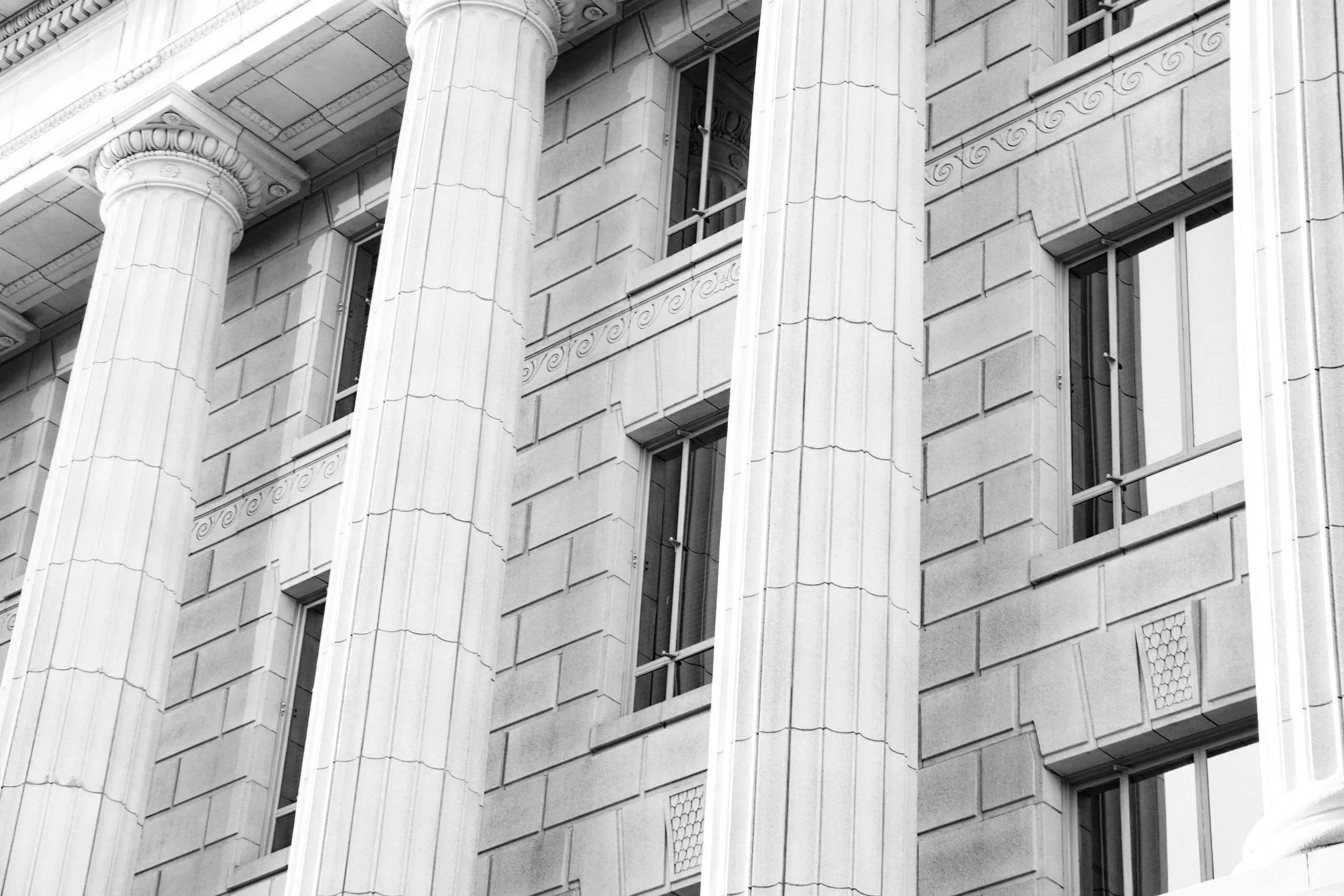 Black and white photo of a building's facade showing tall Corinthian columns and rectangular windows with decorative molding between them.