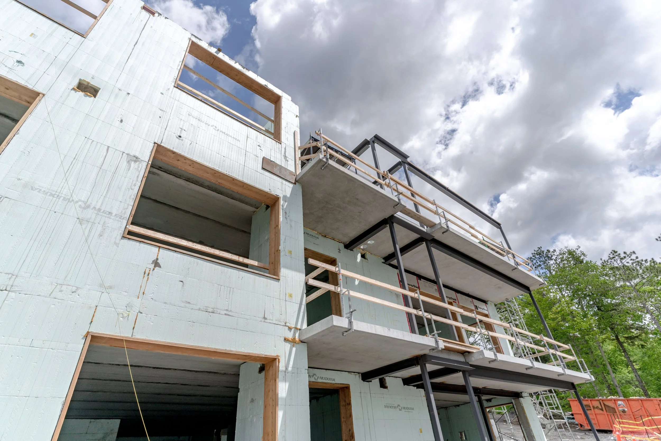 Construction site with a partially built multi-story building, ICF product, scaffolding, and a cloudy sky overhead.