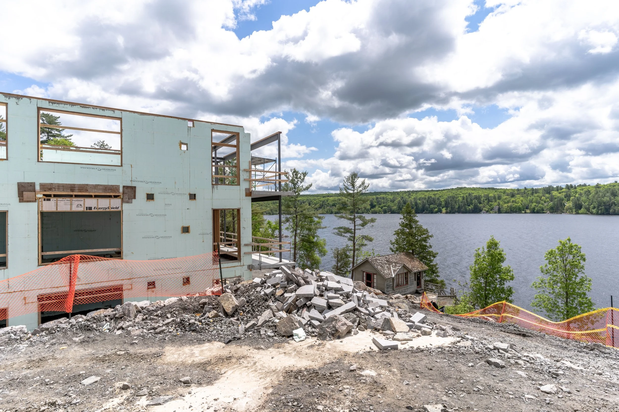 A house under construction with ICF product near a lake with trees and a cloudy sky in the background.