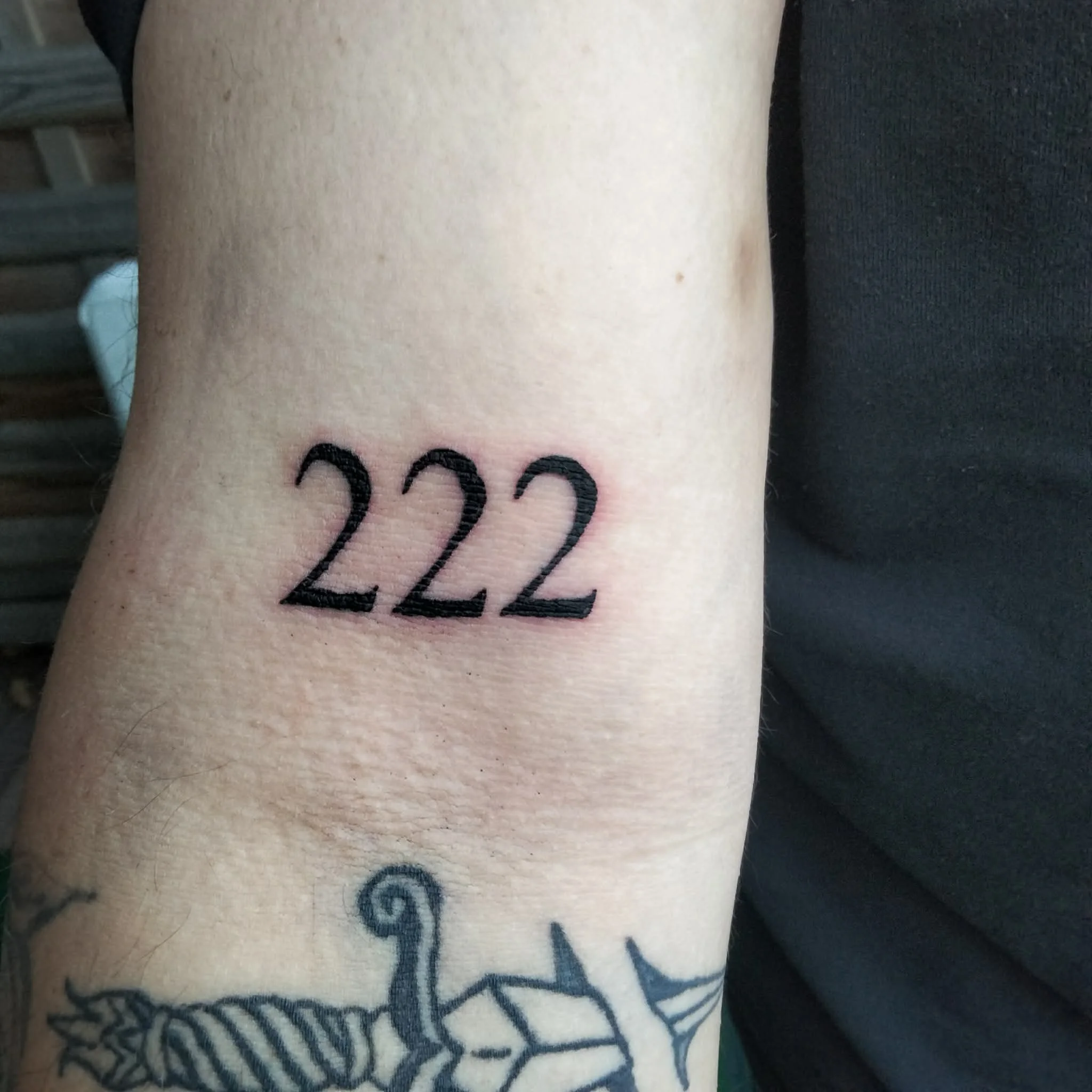 Close-up of a tattoo with black ink on a person's skin, displaying the numbers '222' and additional decorative elements.