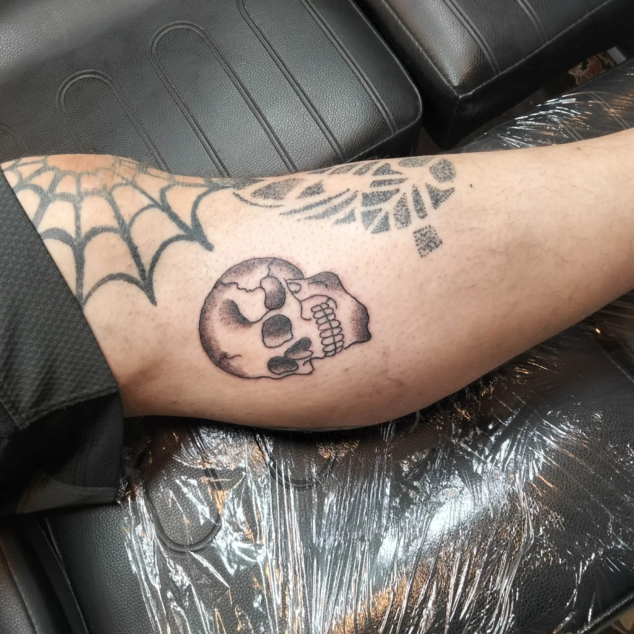 A tattooed arm resting on a black car seat, with a clear plastic covering over the seat.