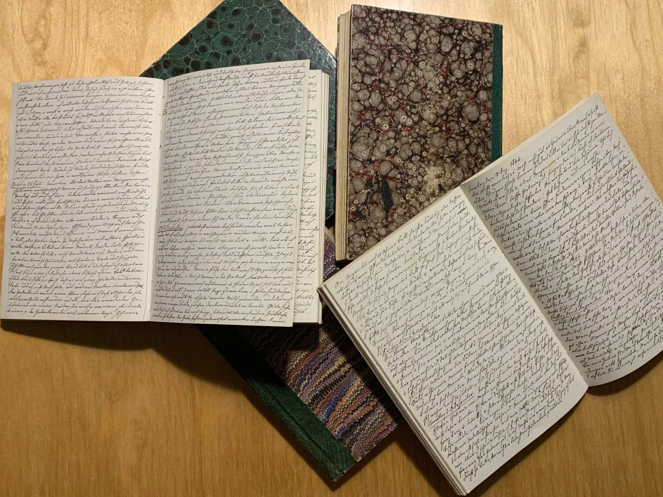 Open books with handwritten text on the pages, on a wooden table.