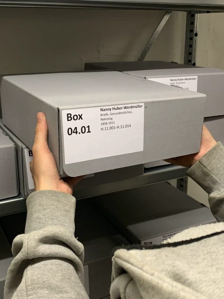 Hands correctly remove a labeled archive box from a shelf using both hands.