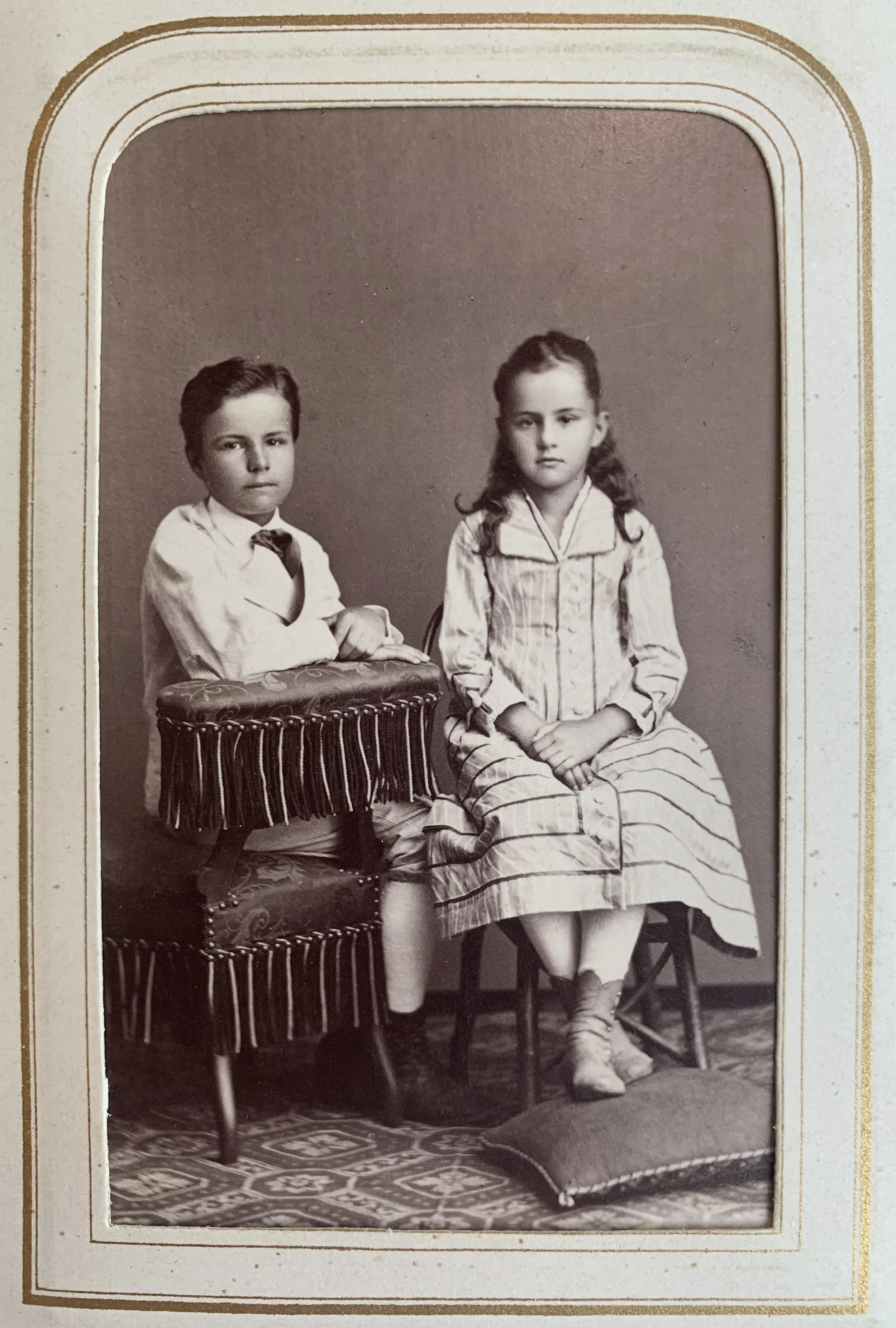 A black-and-white photograph from 1878 showing a boy and a girl sitting in a photography studio. The boy is about 13 years old, and the girl is about 11 years old. They are siblings. The photograph is held in the State Archives of the Canton of Zurich.