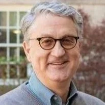 A man with gray hair, glasses, and a friendly smile standing outdoors