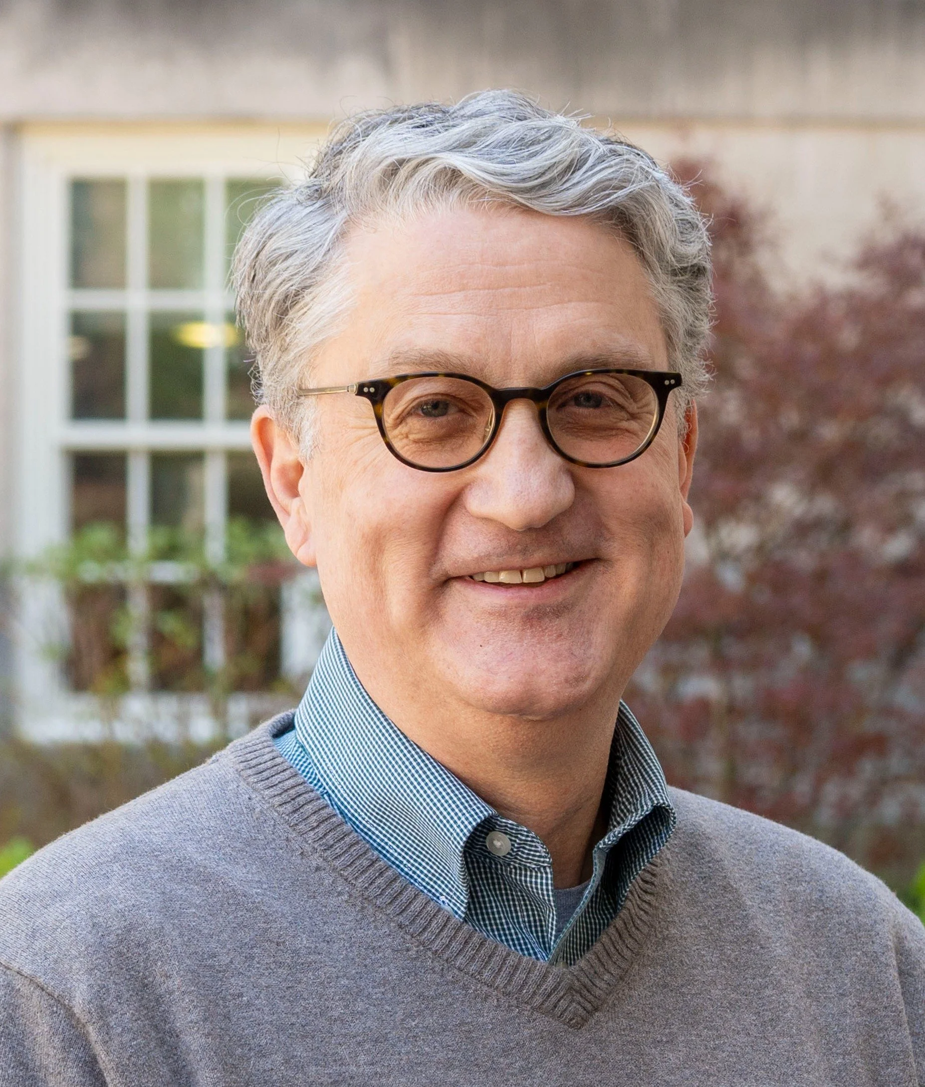 A man with gray hair, glasses, and a friendly smile standing outdoors
