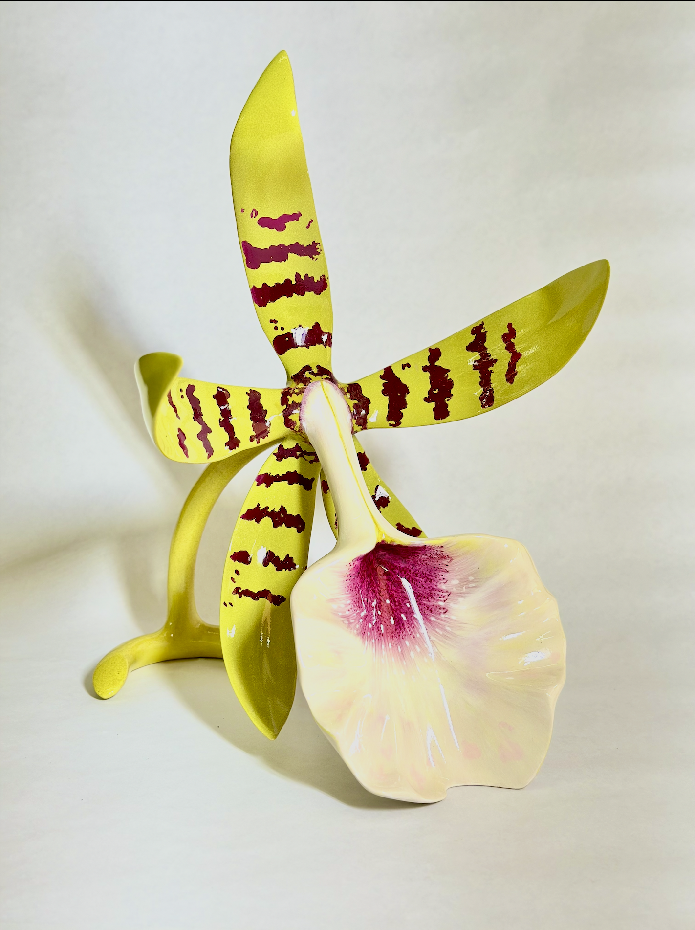 A decorative artificial orchid arrangement with three large yellow petal flowers, each with red markings, and one large light pink and white petal flower with a pink center against a plain off-white background.