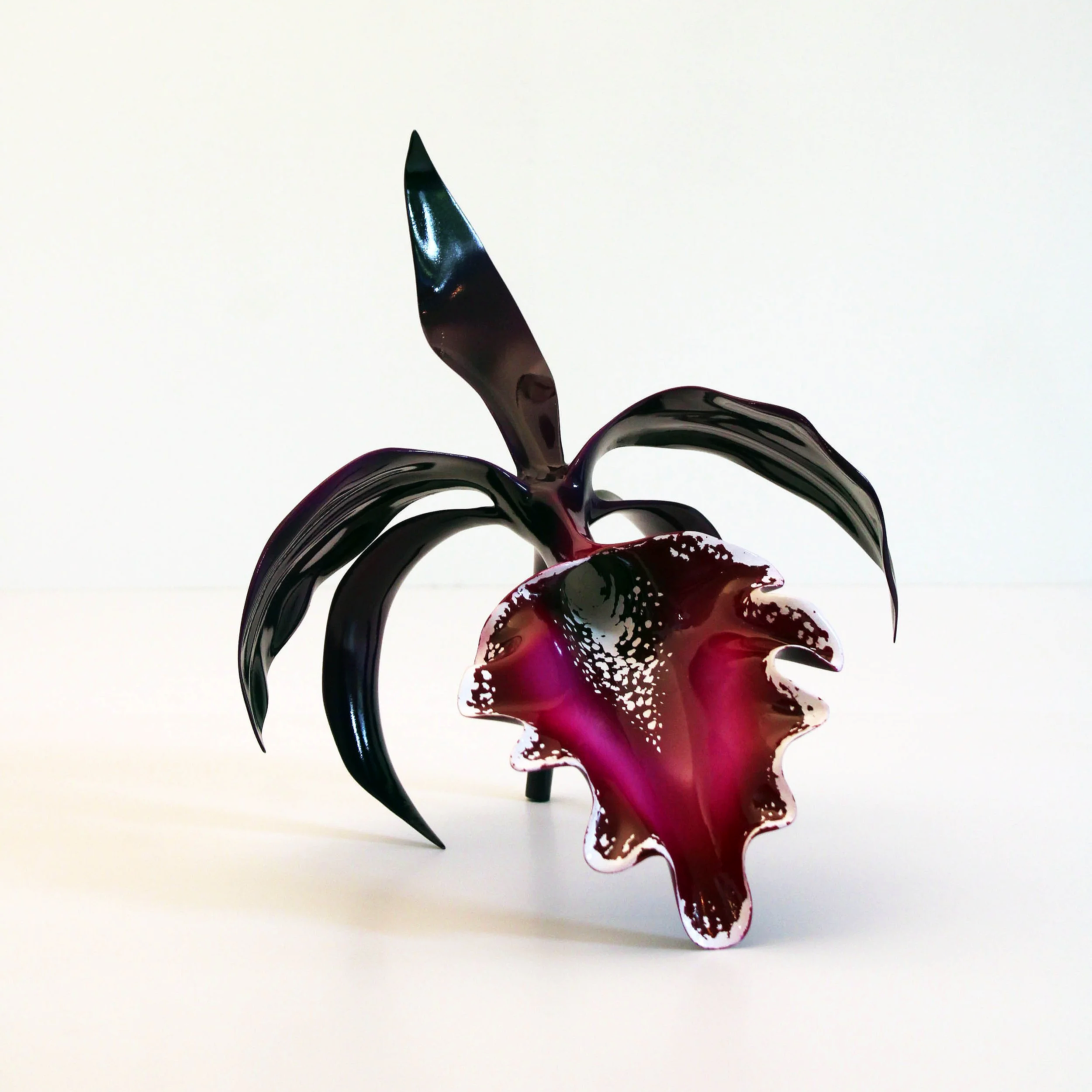 Decorative blown glass sculpture resembling a flower with red and purple petals and dark green leaves against a plain white background.