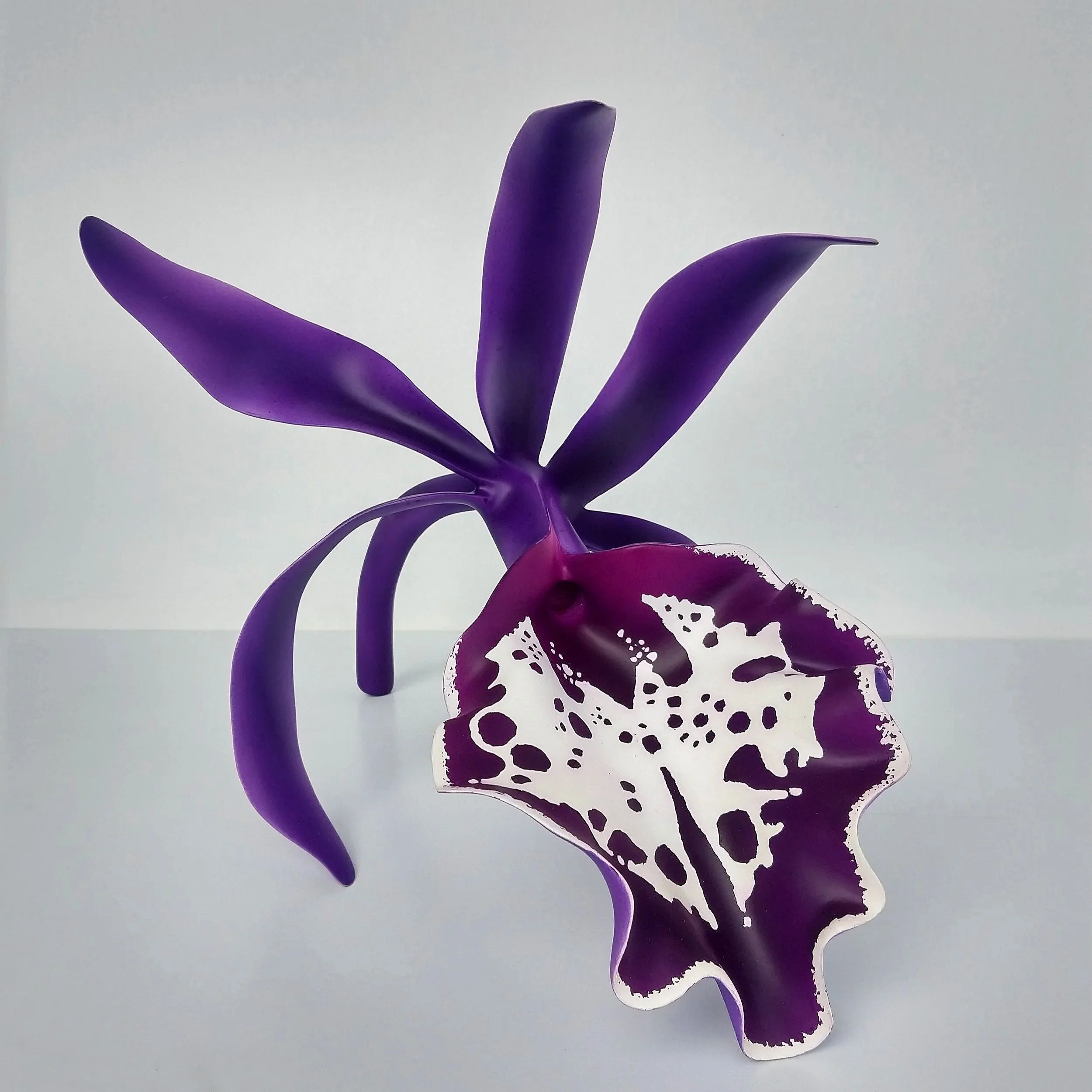 A decorative purple and white paper cutout of a flower with three purple petals and a white and purple patterned leaf, set against a plain white background.
