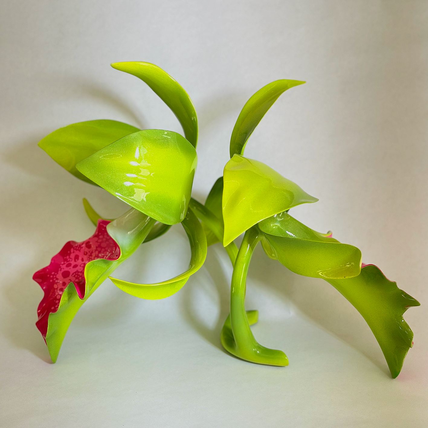 Colorful artificial plant with green leaves and pink accents on a plain backdrop.