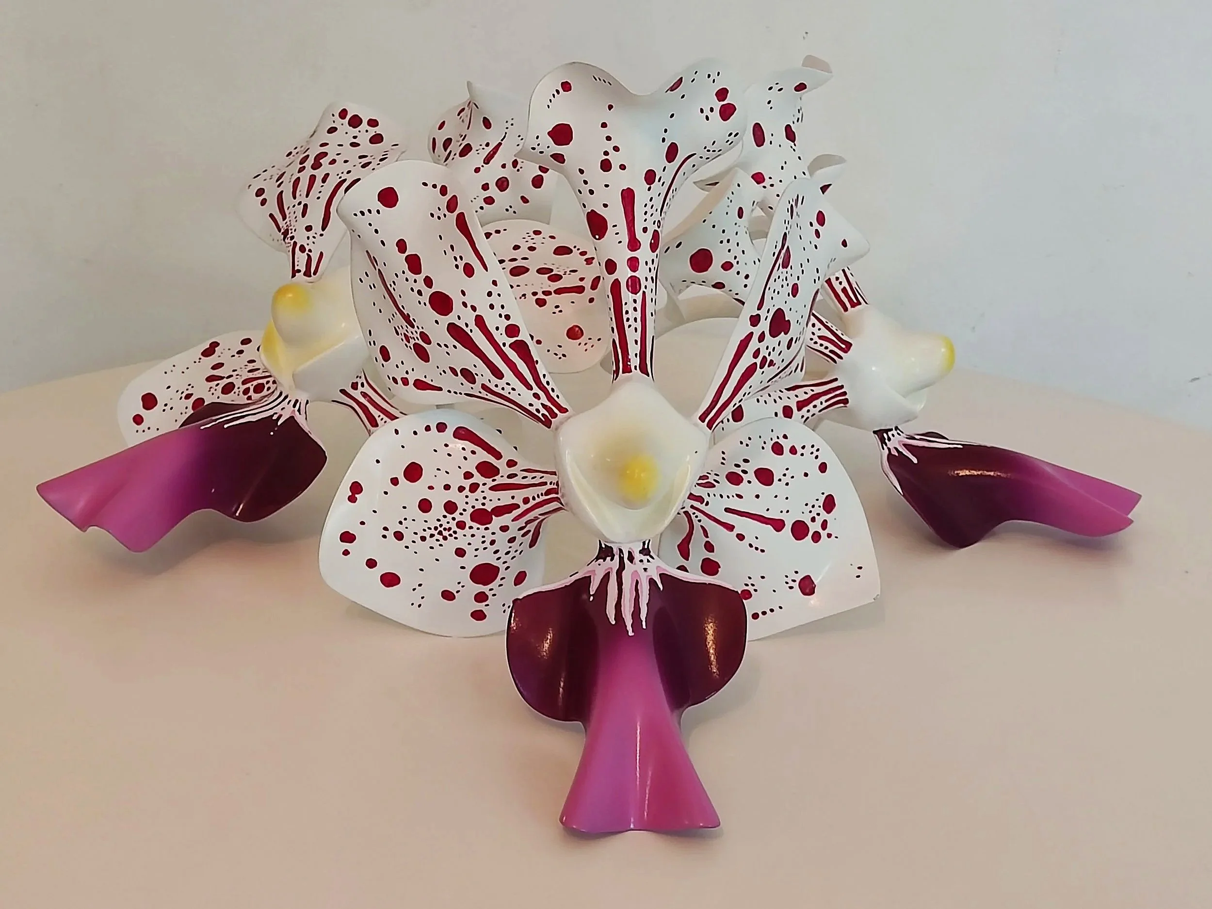 Decorative sculpture of a white orchid flower with purple petals and red speckles, attached to a pink vase.