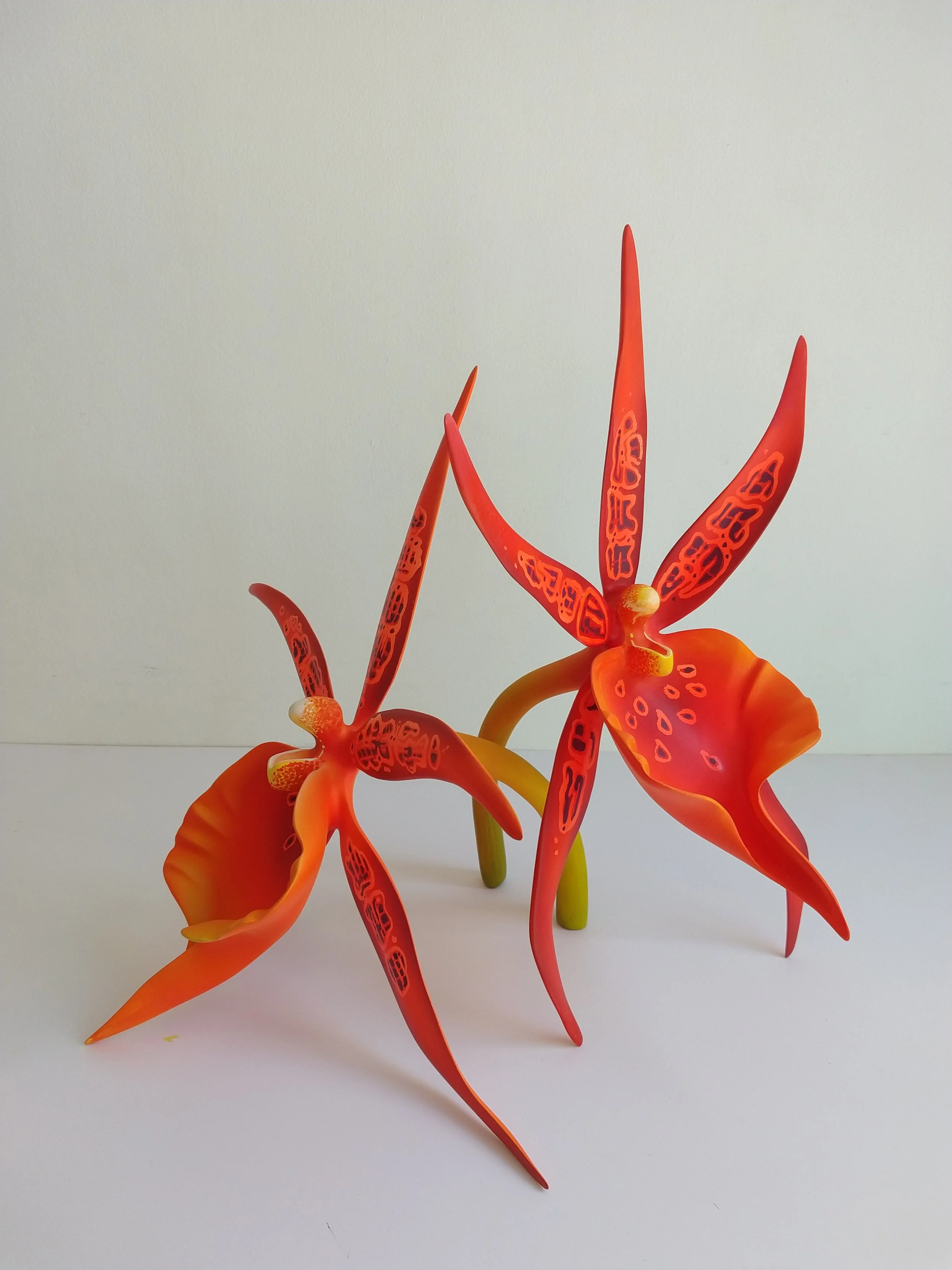 Colorful glass sculpture resembling a flower with elongated red and orange petals and green stems, set against a white background.