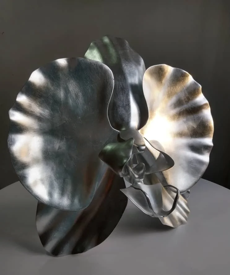 Abstract metal sculpture resembling butterfly wings with reflective silver, black, and white surfaces on a gray platform.
